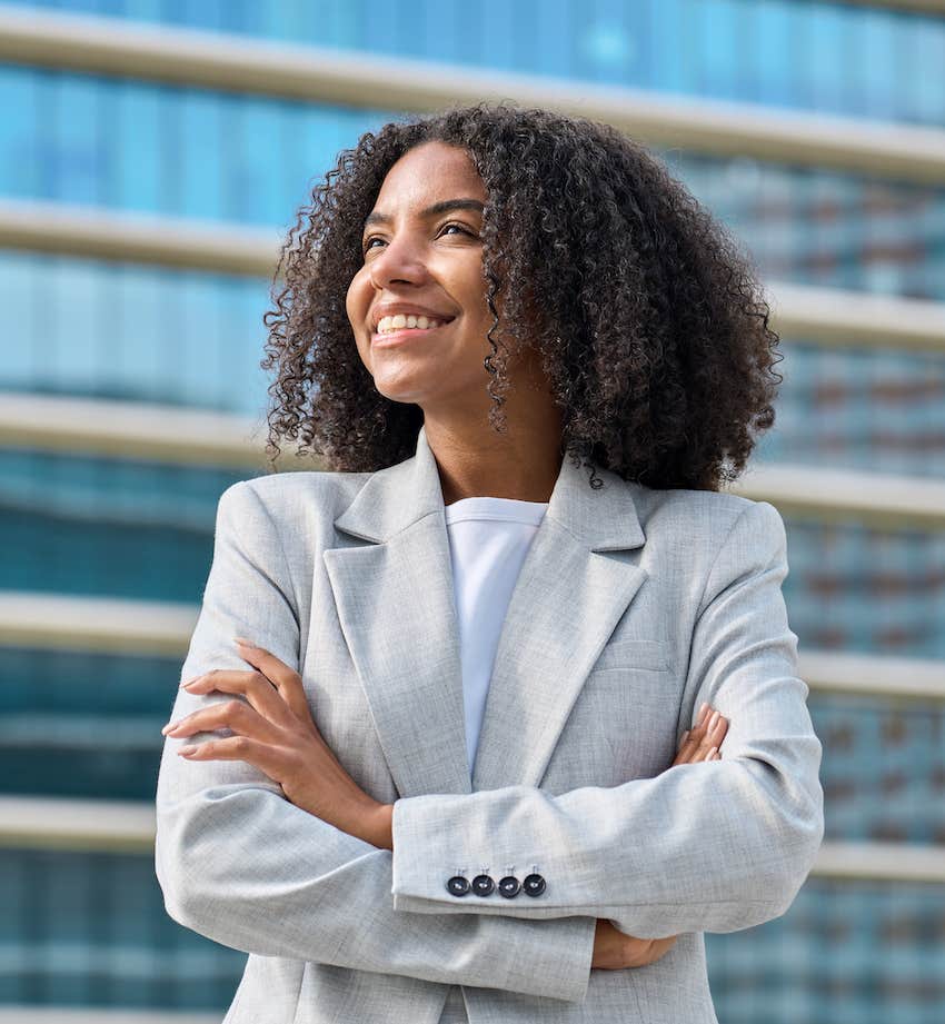 Confidently smiling woman crosses her arms in front of office buidling