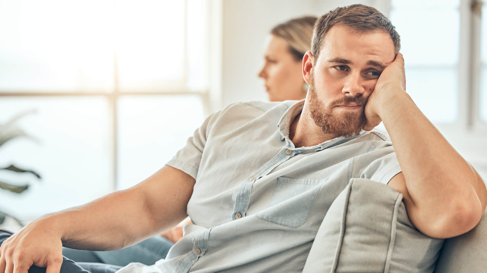 Upset man turned away from his wife on the couch