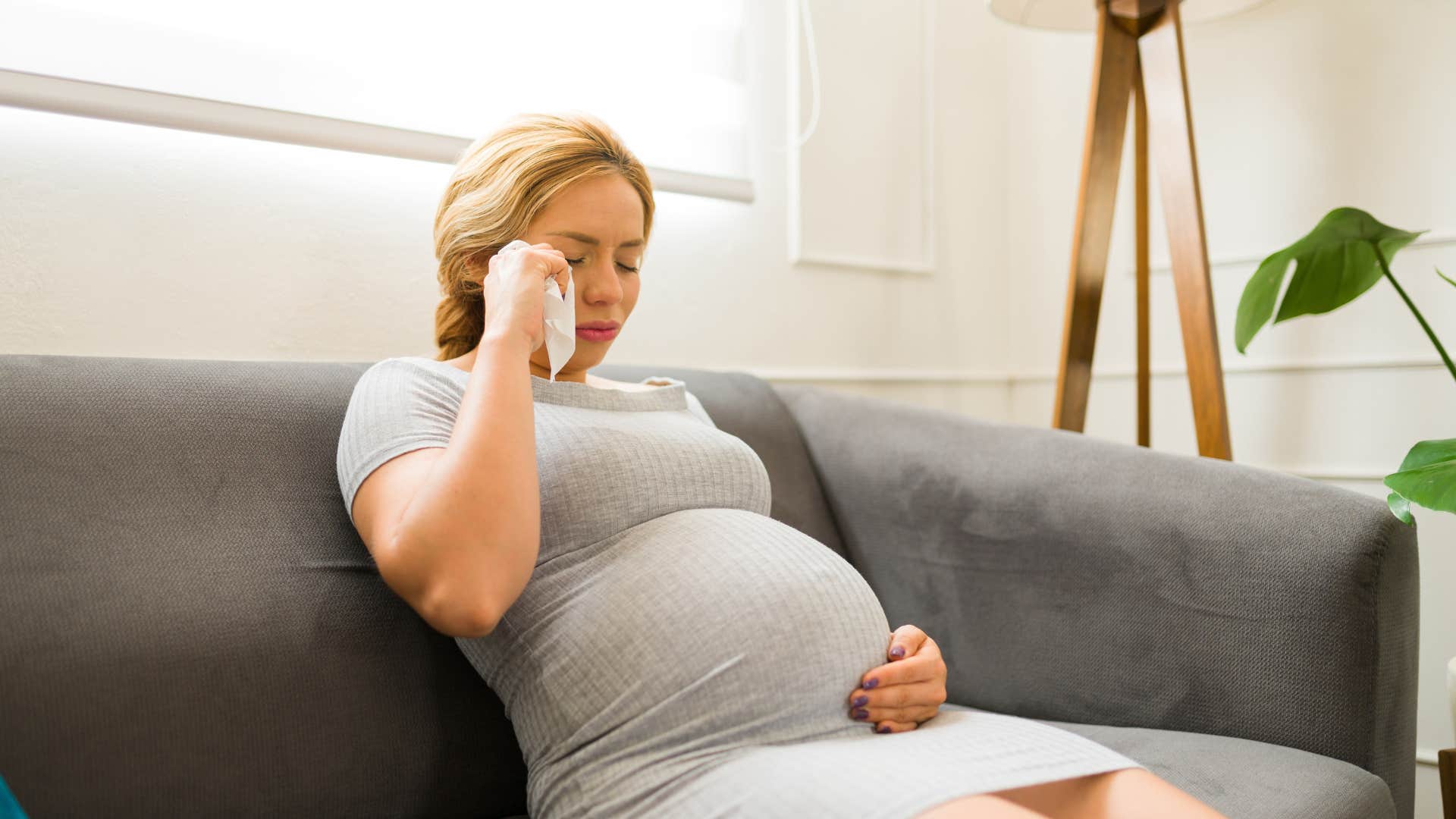 pregnant woman sitting on couch crying