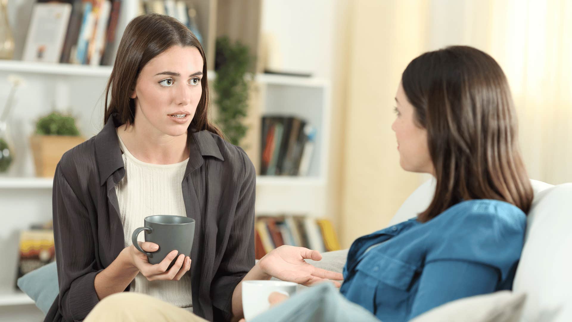 friend talking to other friend while drinking coffee on the couch