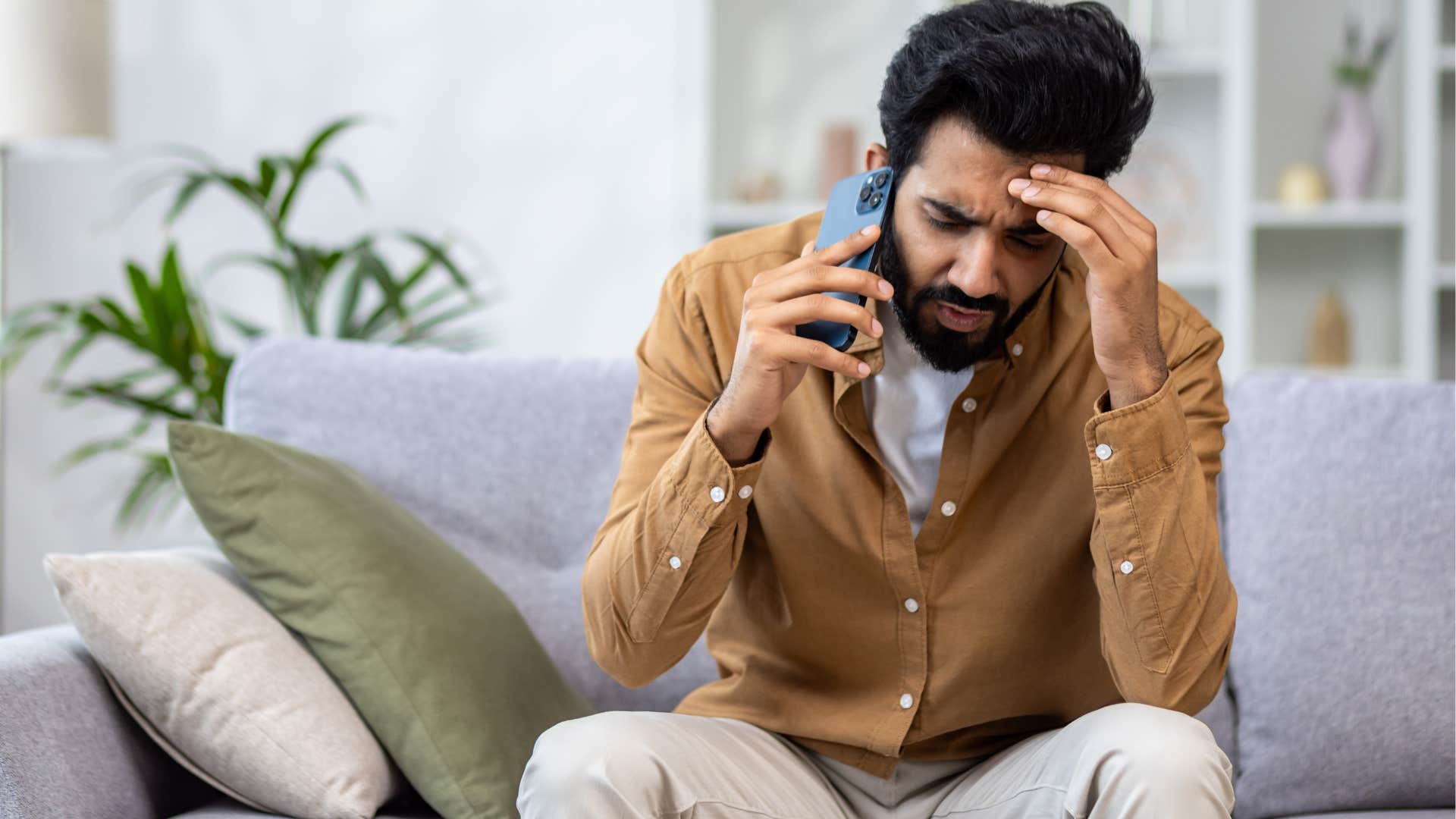 Upset man holding his head while talking on the phone.