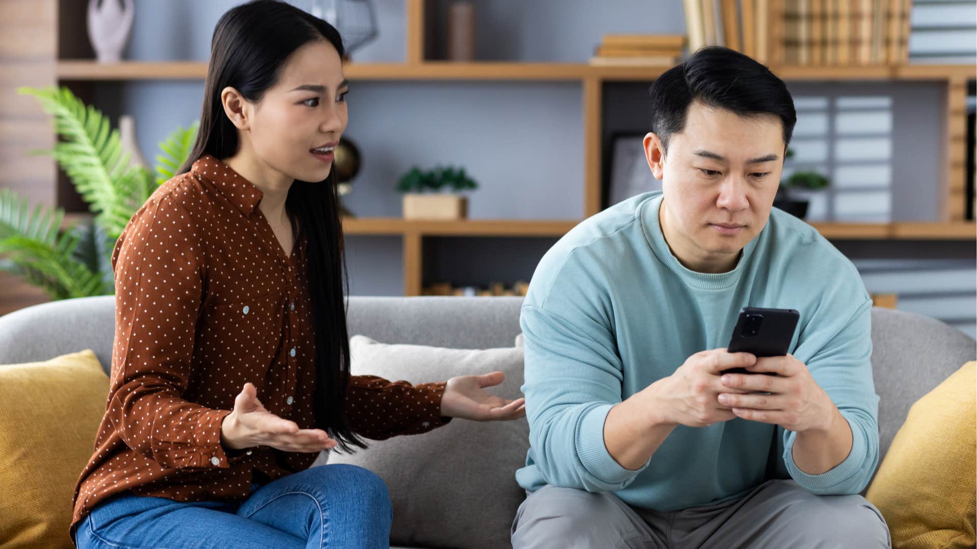 Woman arguing with her distracted boyfriend on the couch.