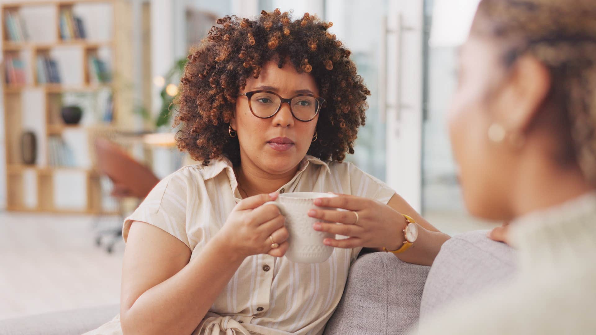 Annoyed woman drinking coffee and listening to her talking friend.