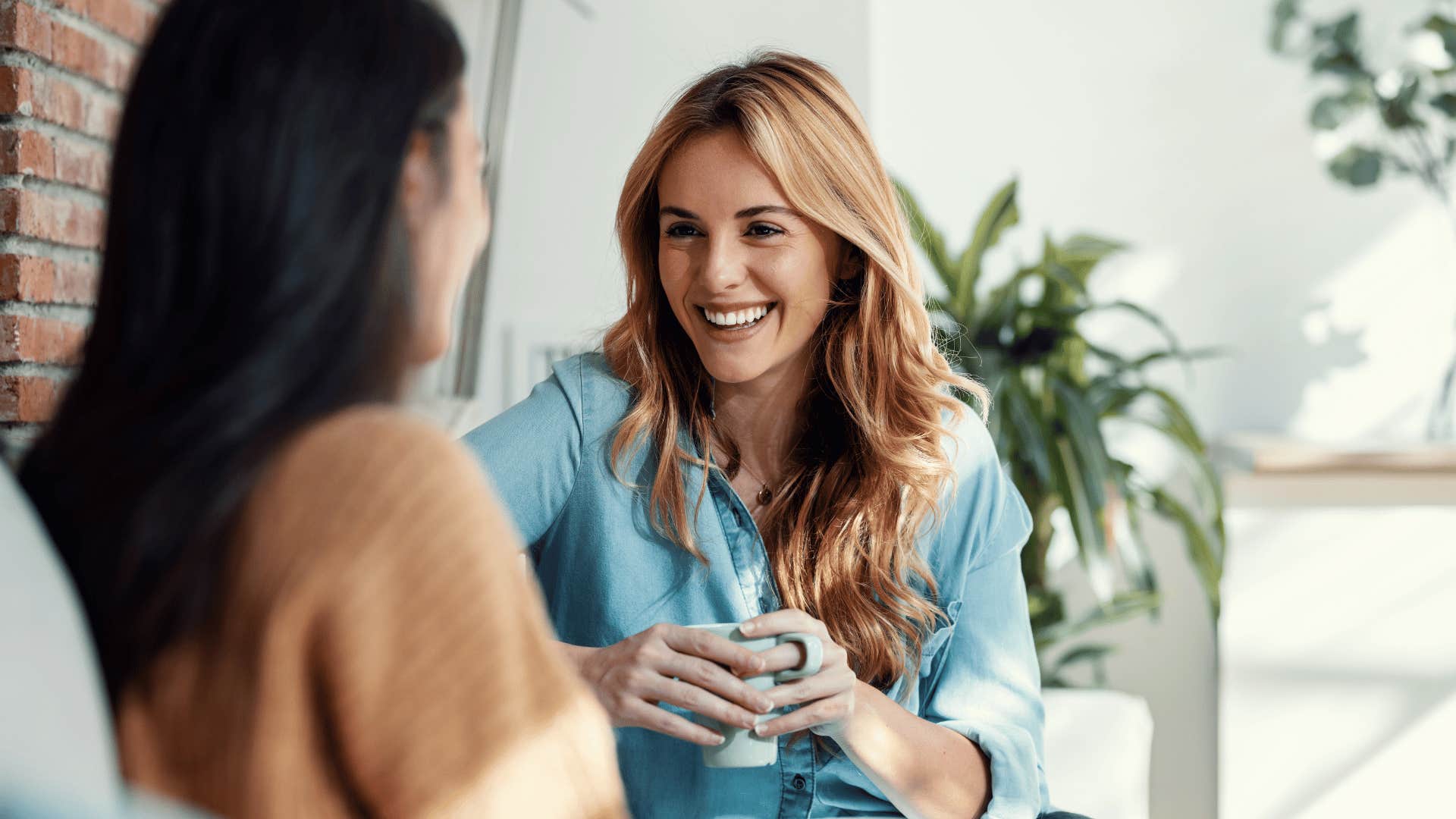 two women chatting on the couch while smiling 