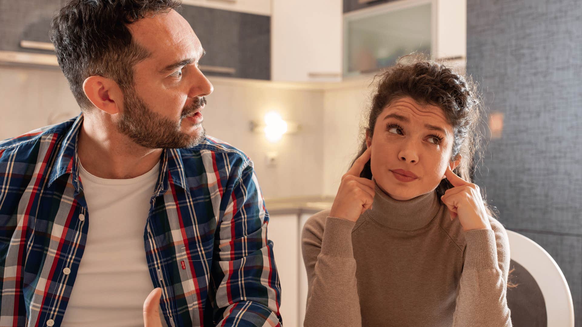 woman covering her ears while man talks