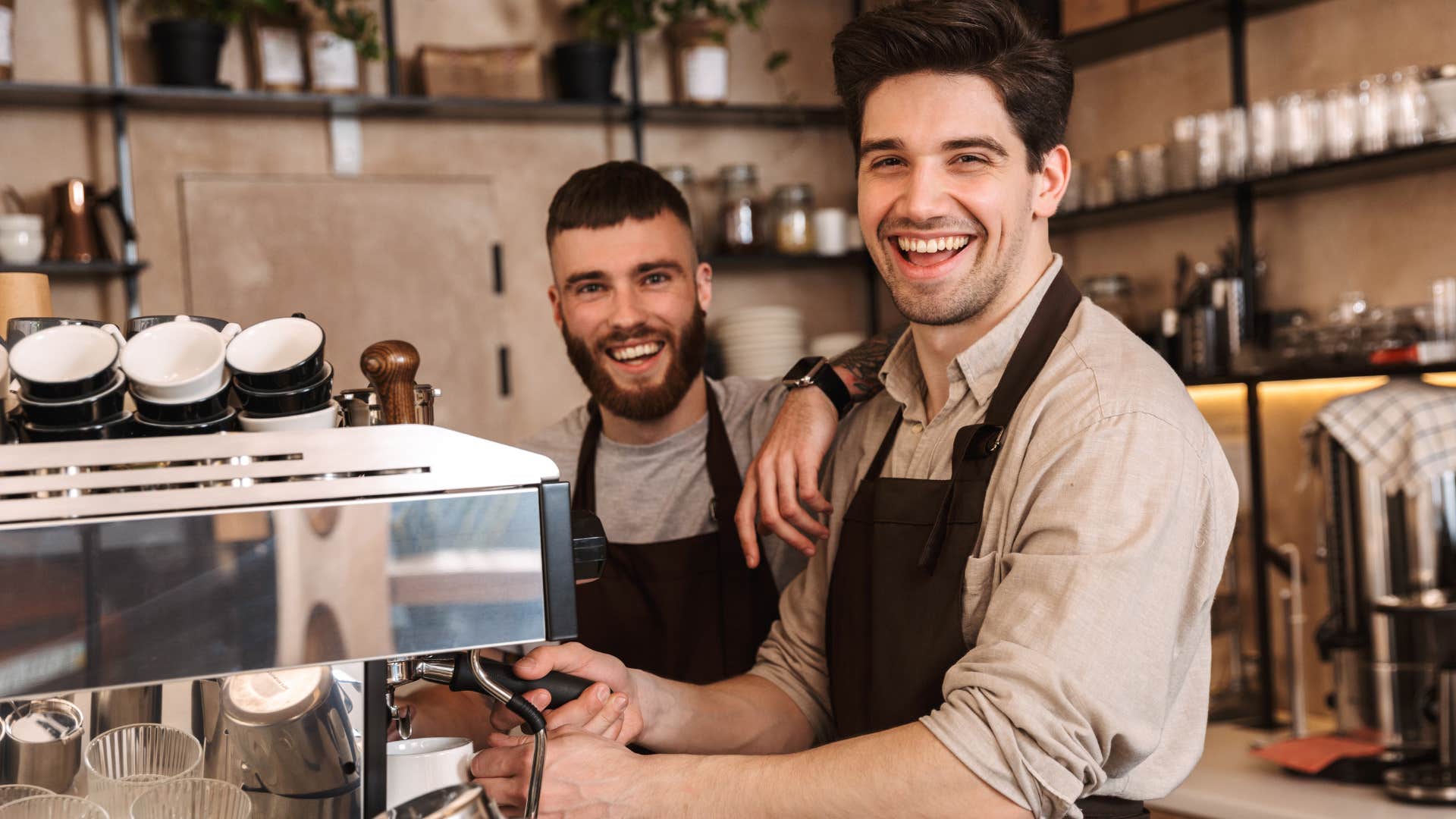 Two men smiling and working at a coffee shop together.