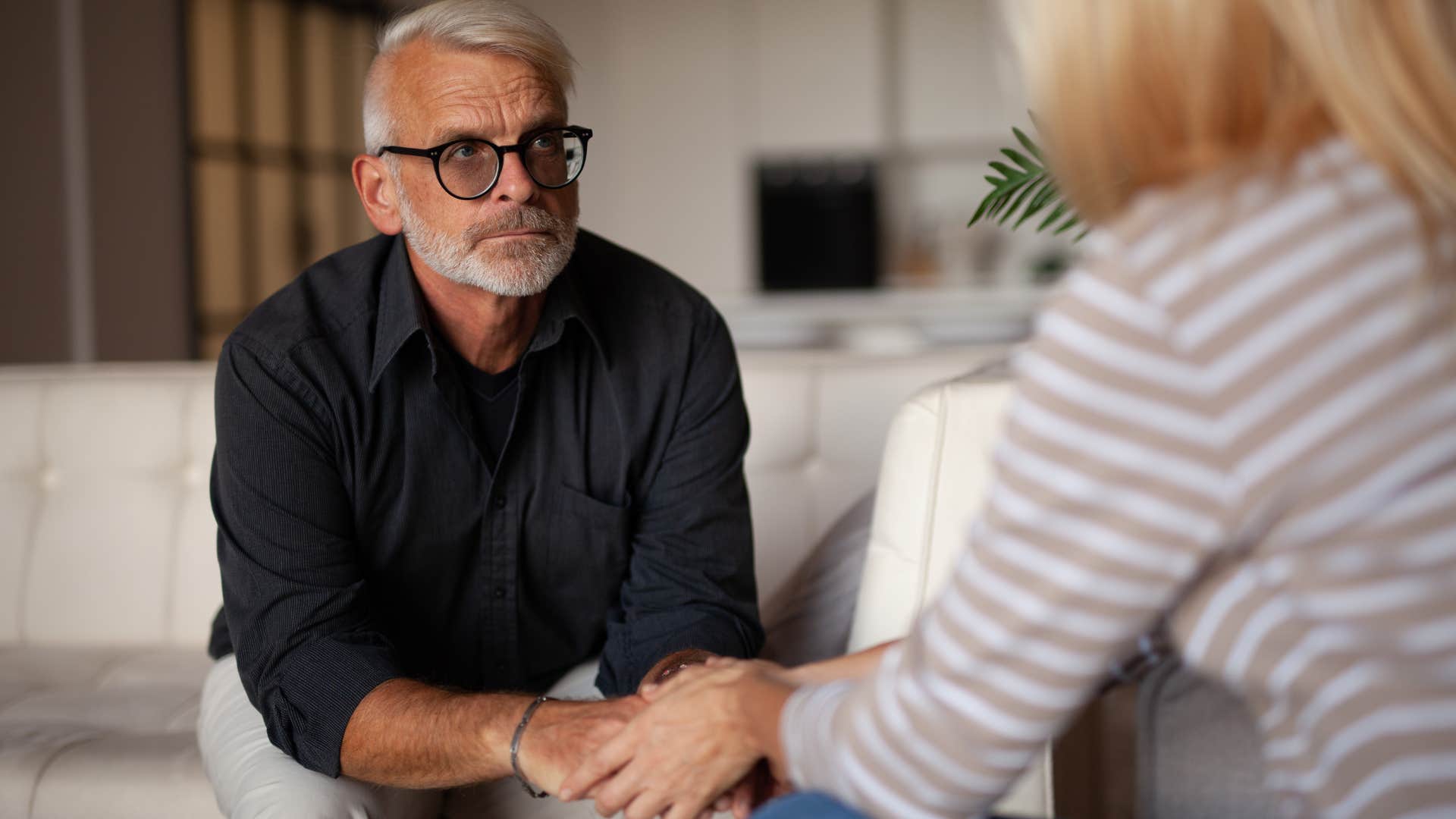 Older man looking serious holding his partner's hands.