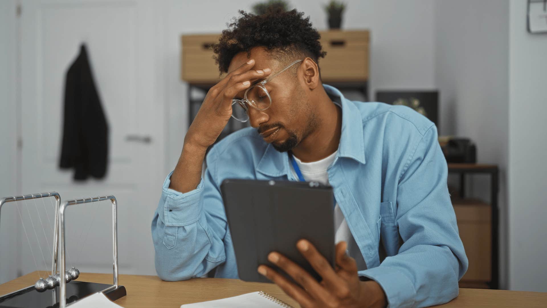 man putting head in hand while looking at laptop