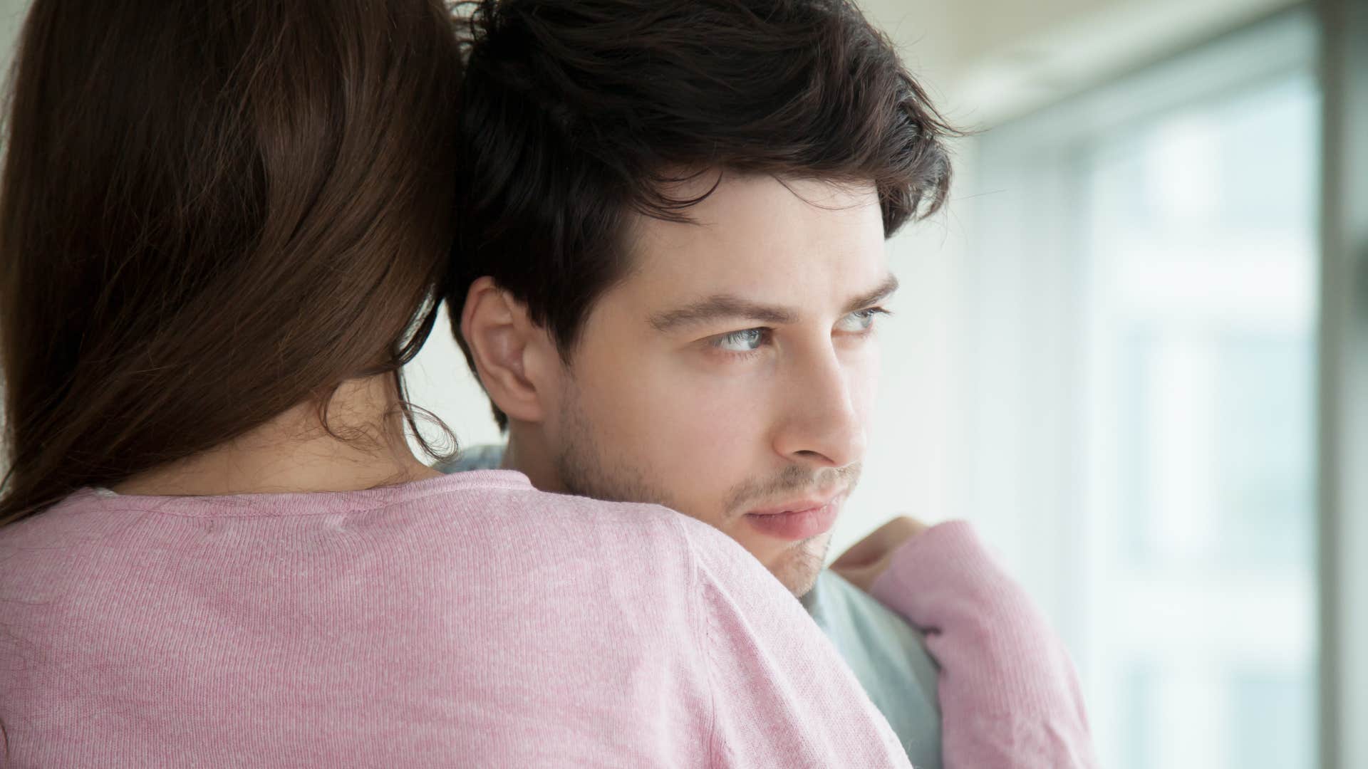 Man looking annoyed while hugging a woman