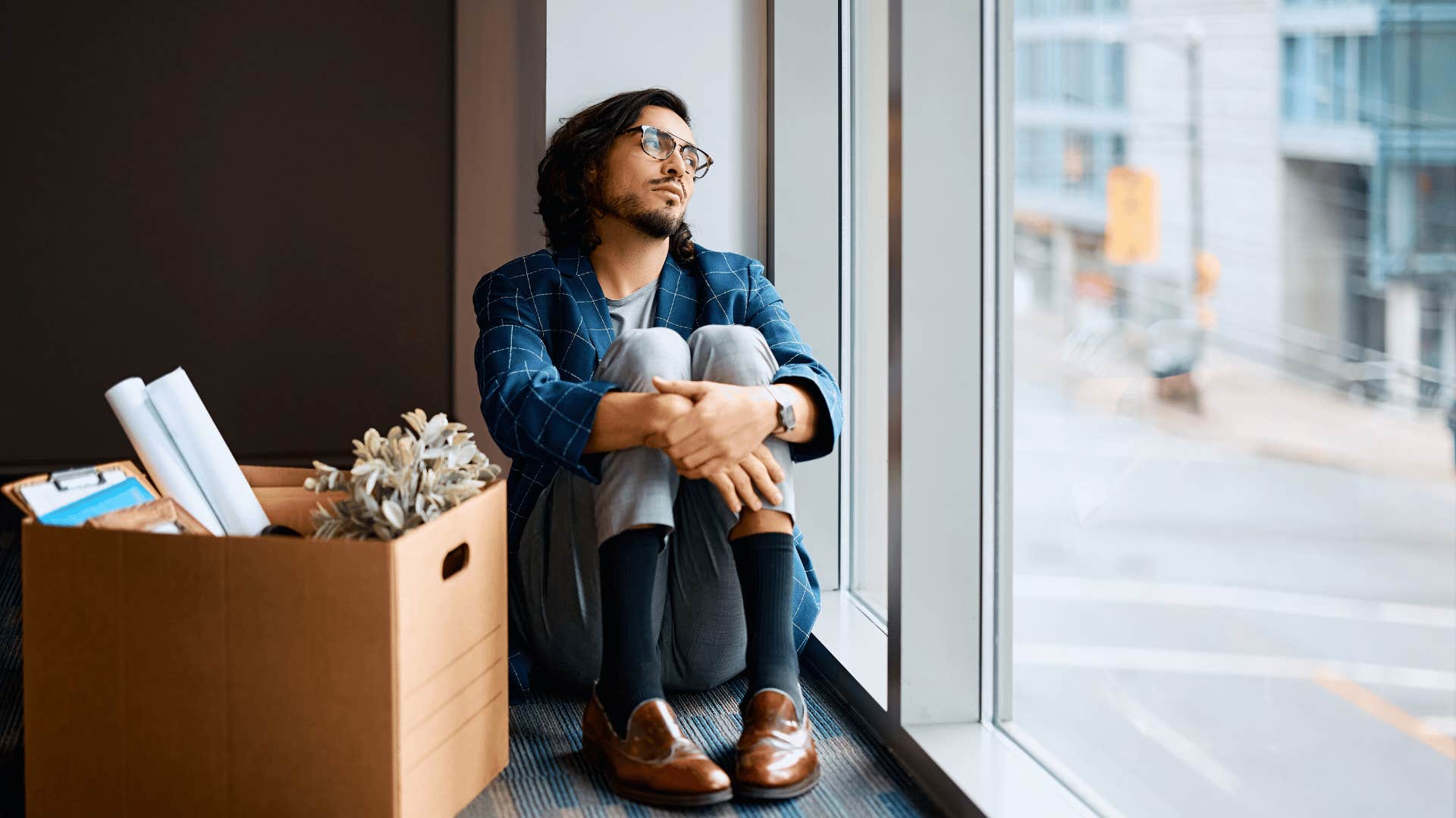 man sitting next to box staring sullenly out the window