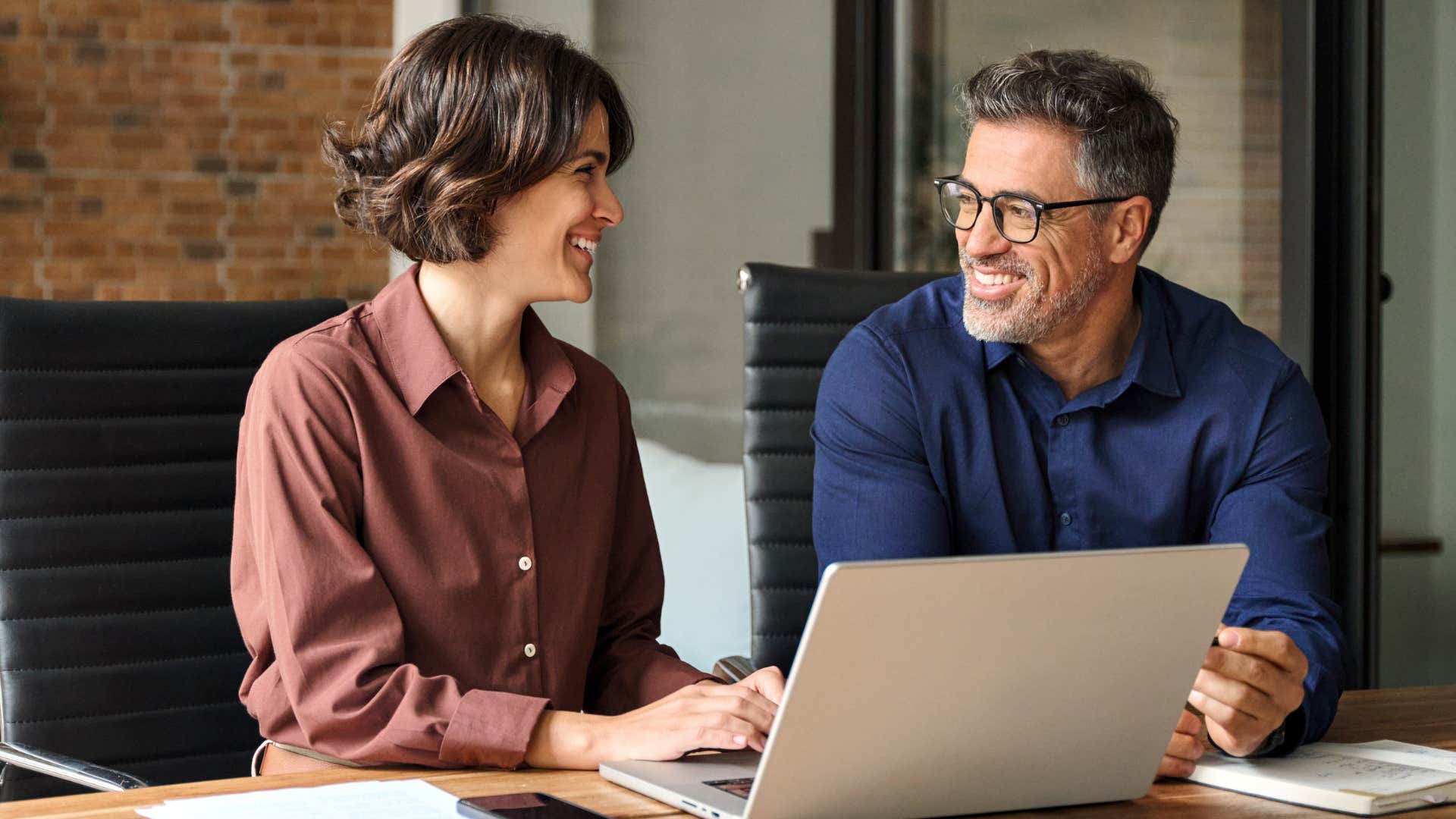 Co-workers smiling and talking at their desk