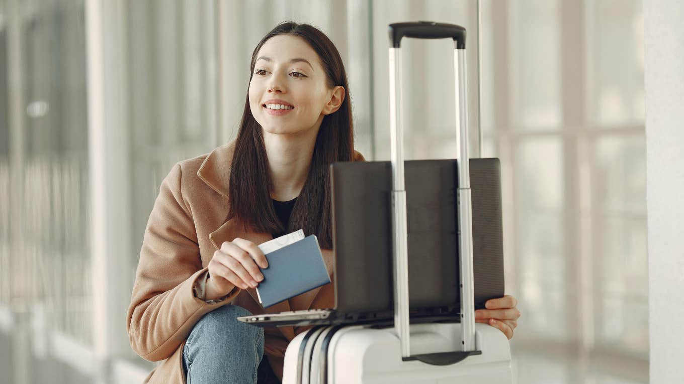 Woman with passport using laptop on luggage in airport