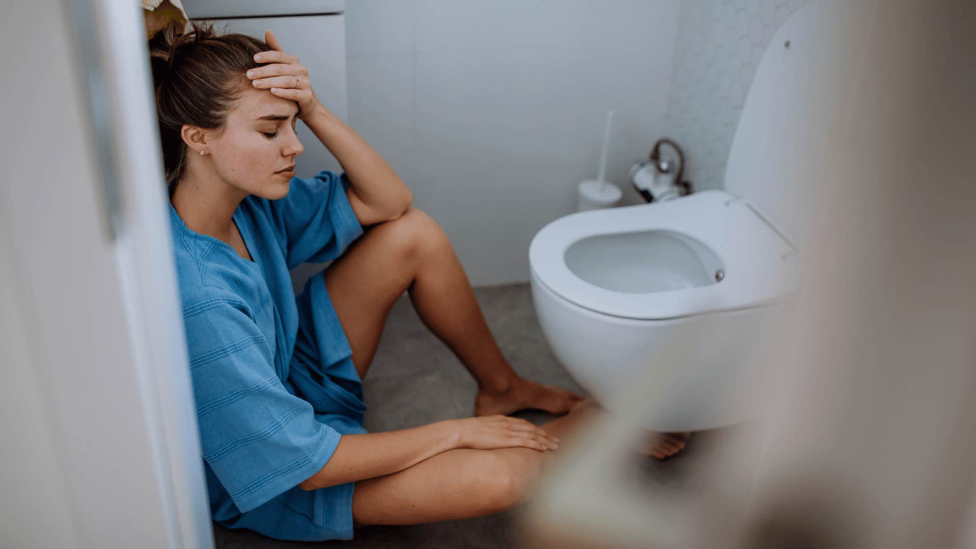 Young sick woman sitting on floor near toilet.