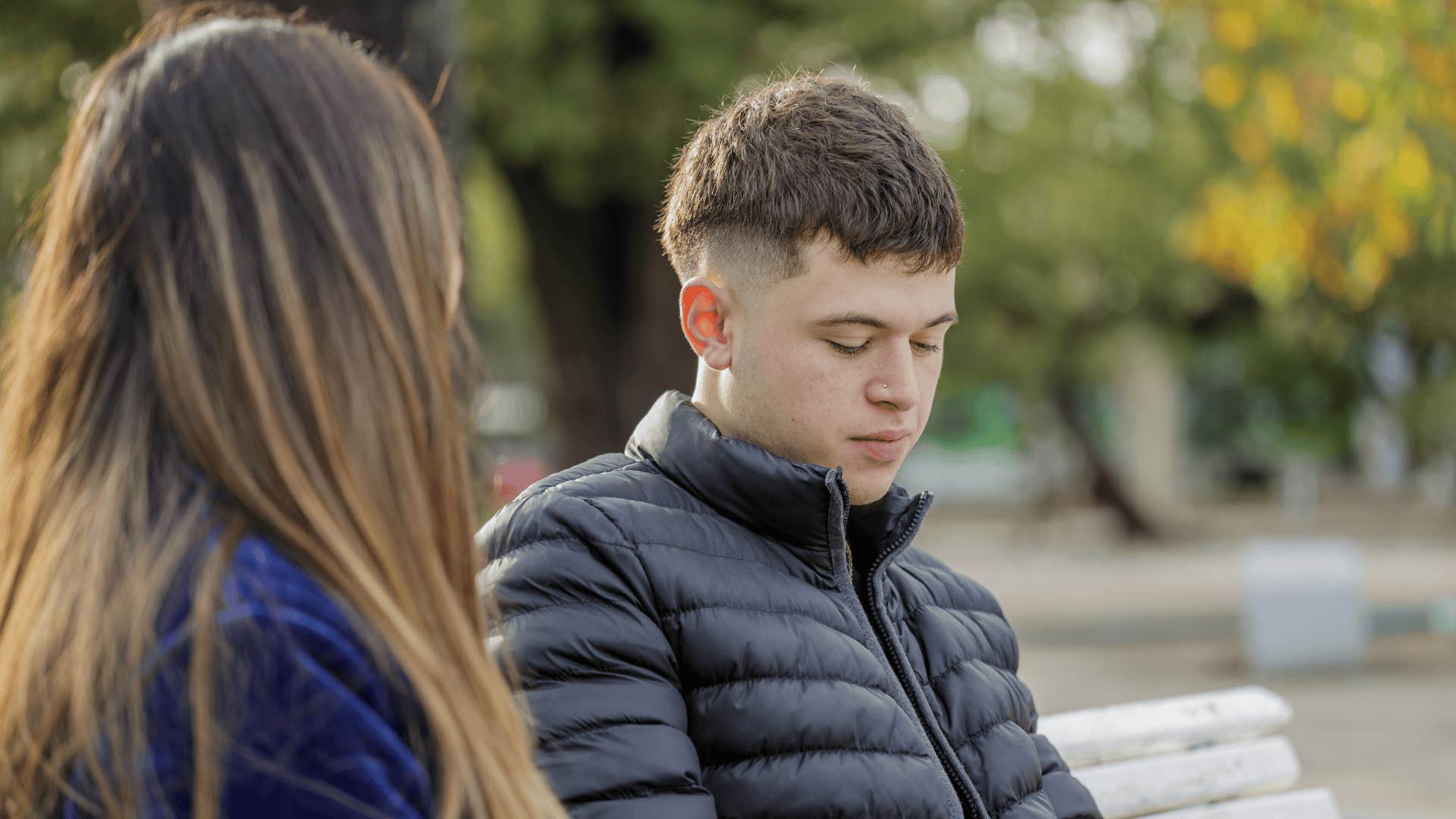 Boy with a melancholic gesture sitting on a bench in the square next to a girl.