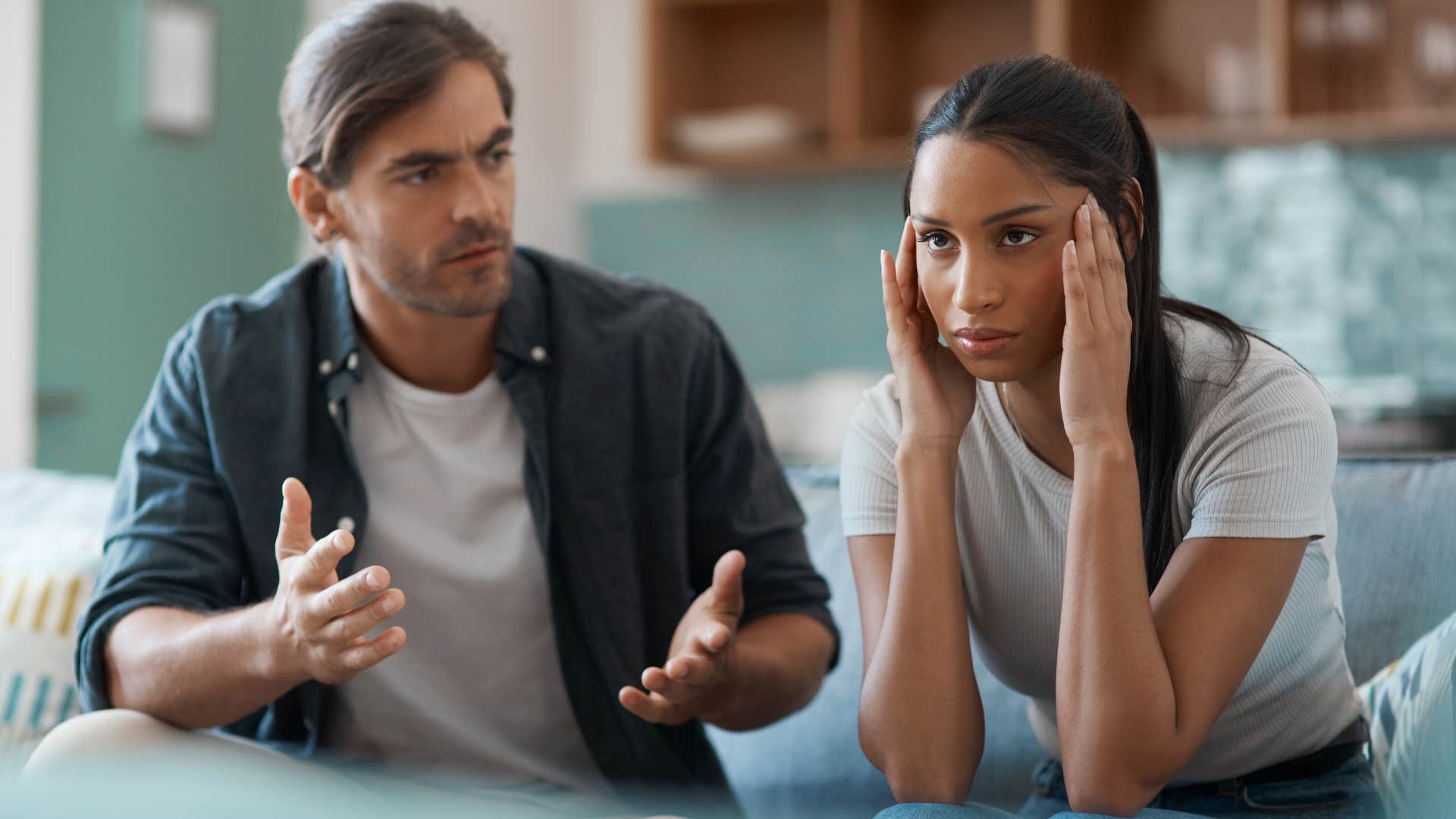 Man arguing with his upset partner on a bed.