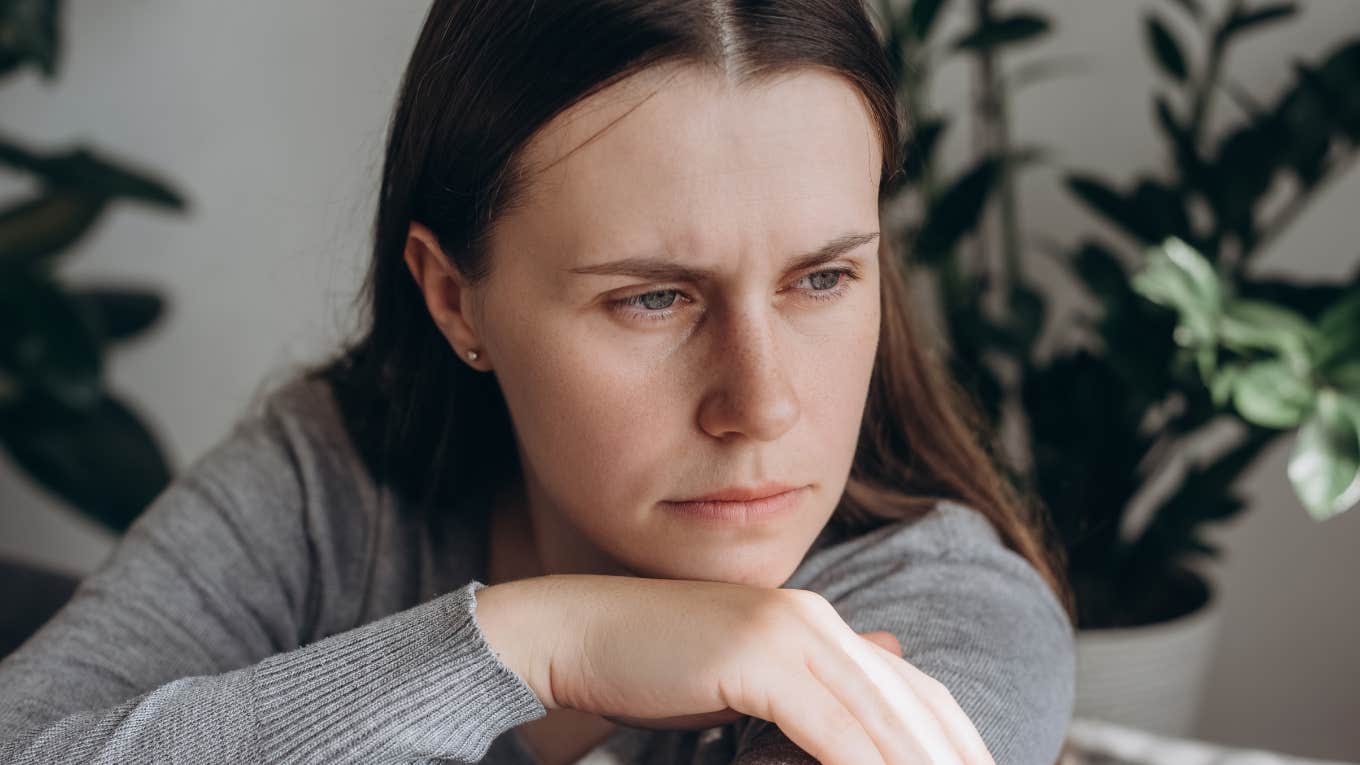 Upset woman leaning her head in her hands and looking out a window.