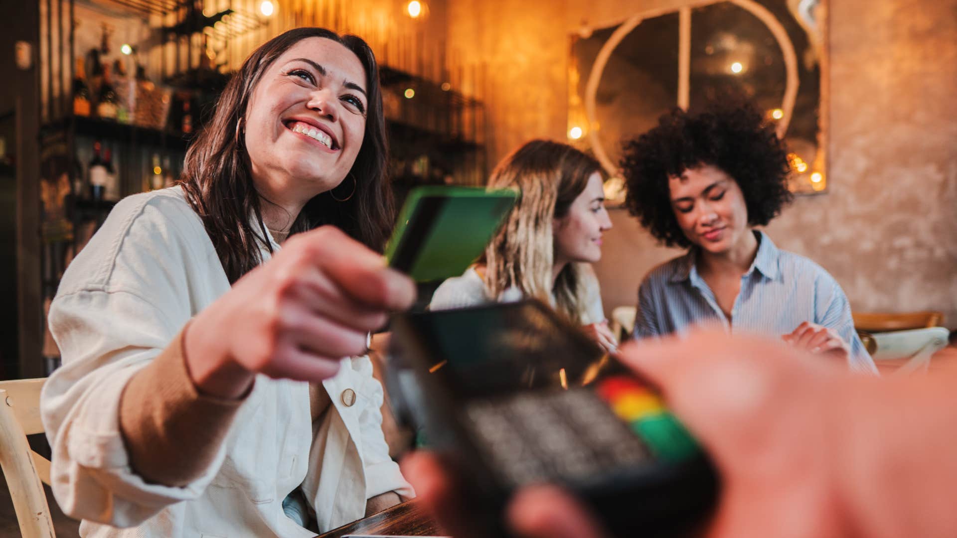 Happy young woman paying bill with a contactless credit card in a restaurant