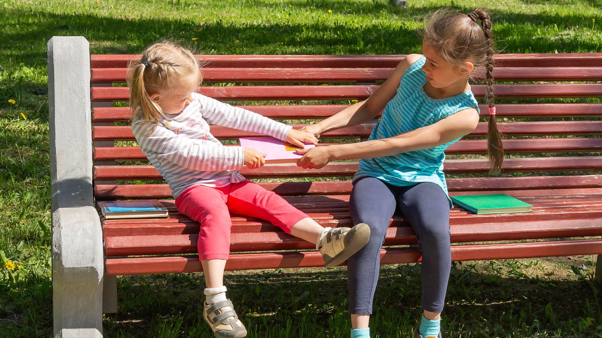 little girl refusing to share books with friend