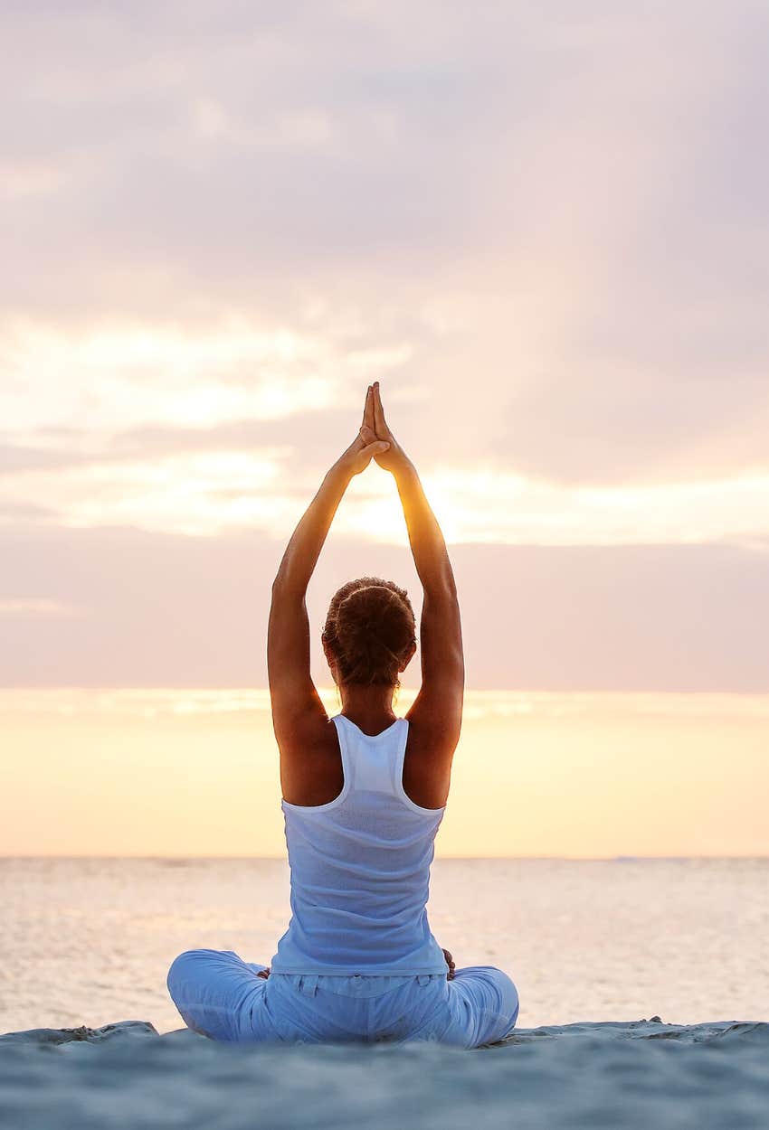 woman practicing yoga on a beach at sunrise