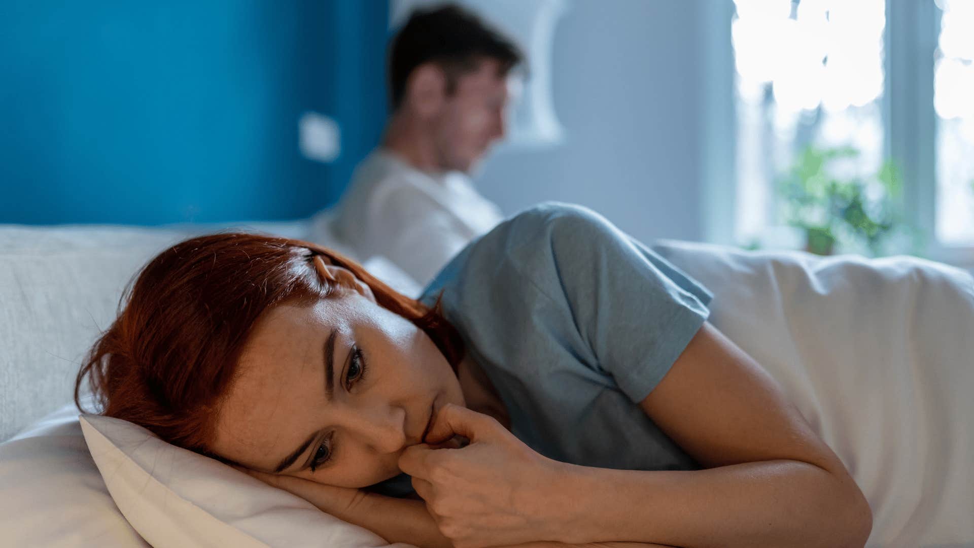 woman lying in bed with her back turned towards man