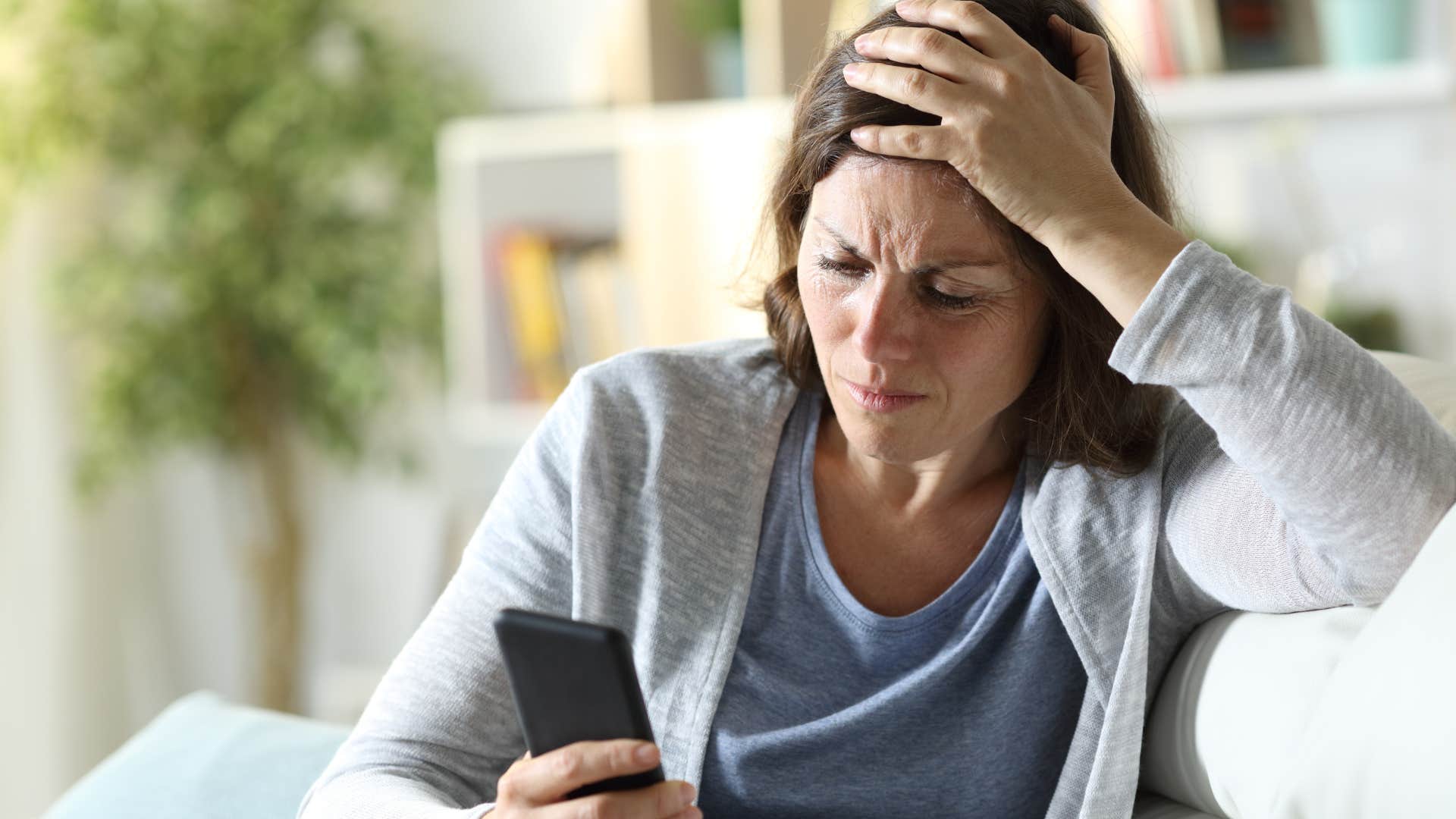 Woman holding her head and looking anxious at her phone.