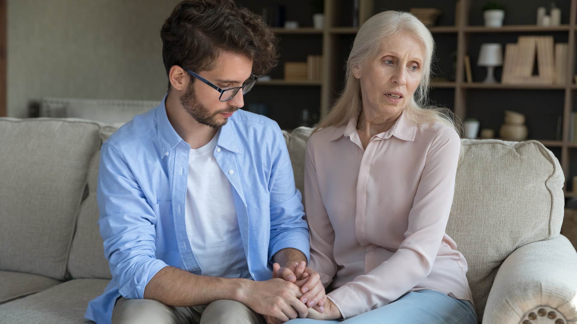 Man comforting his upset adult mother on the couch.