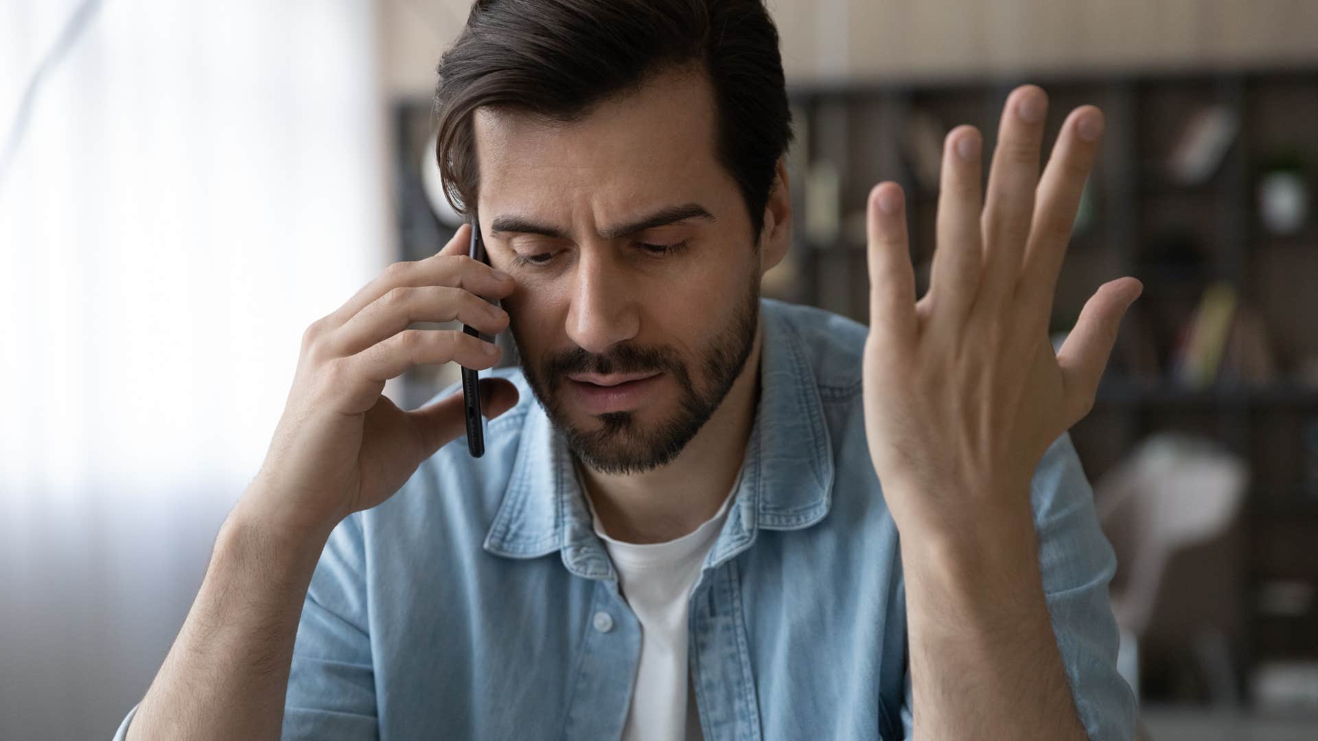 Confused man holding his hands up while talking on the phone.