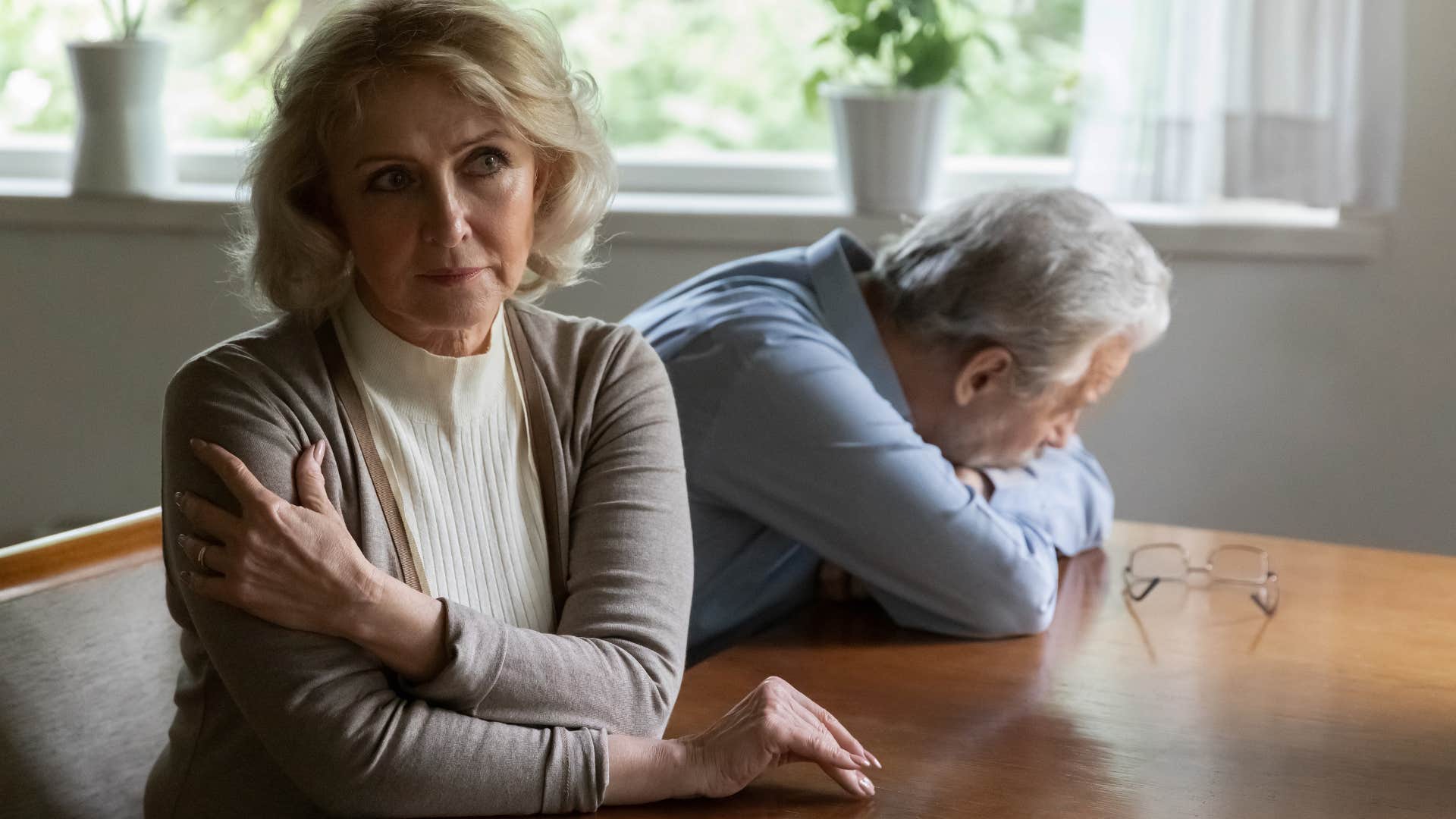 Older woman turned away from her upset husband at a table.