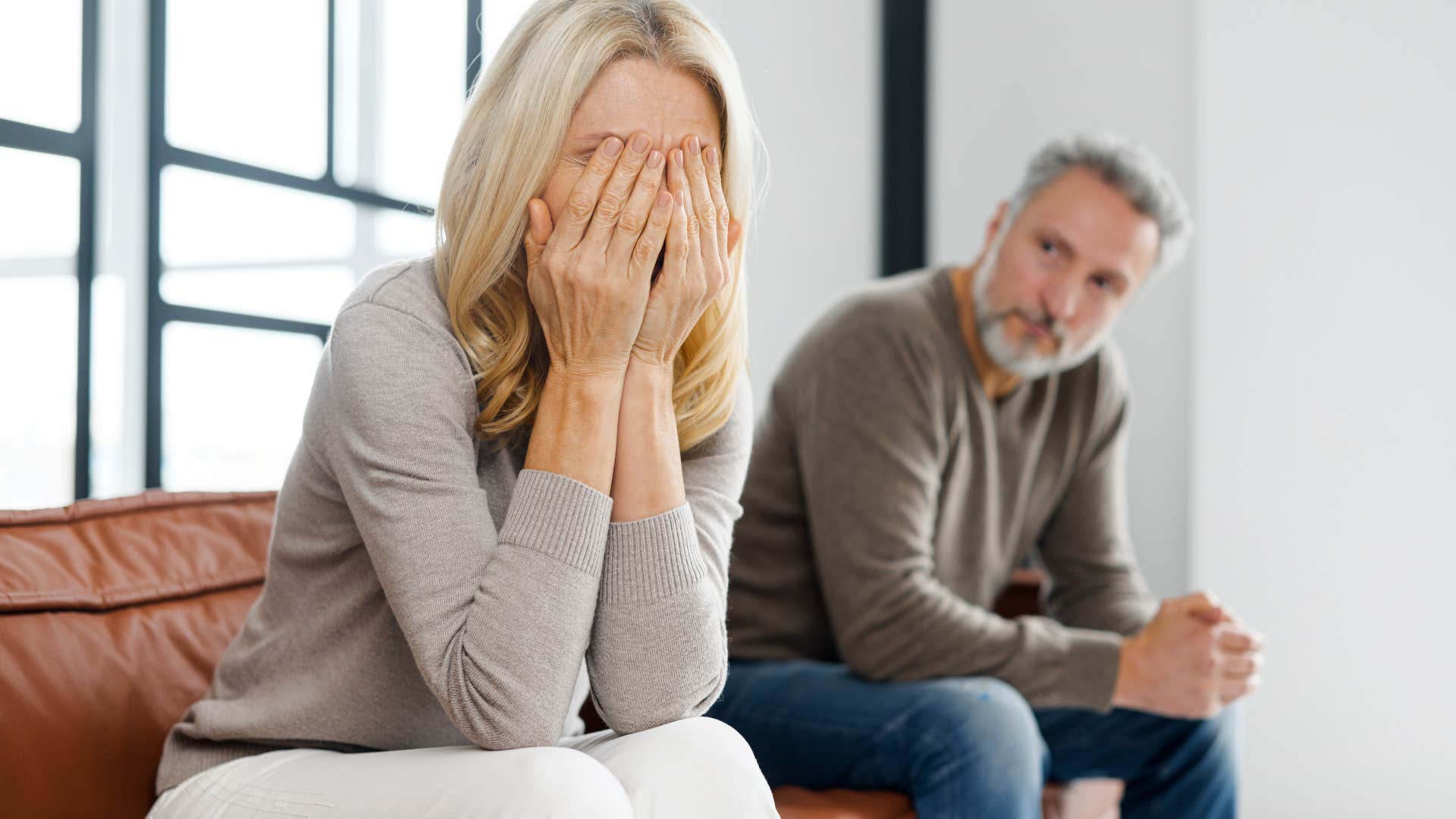 Older woman holding her head in her hands in front of her husband.