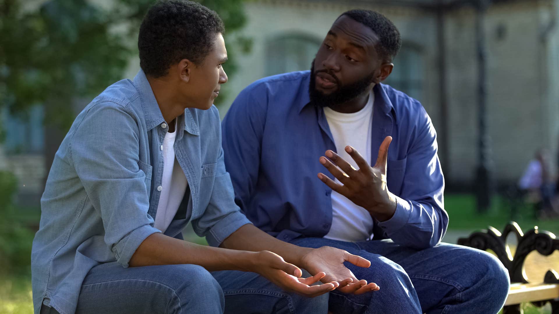 Father talking to his adult son on a park bench.