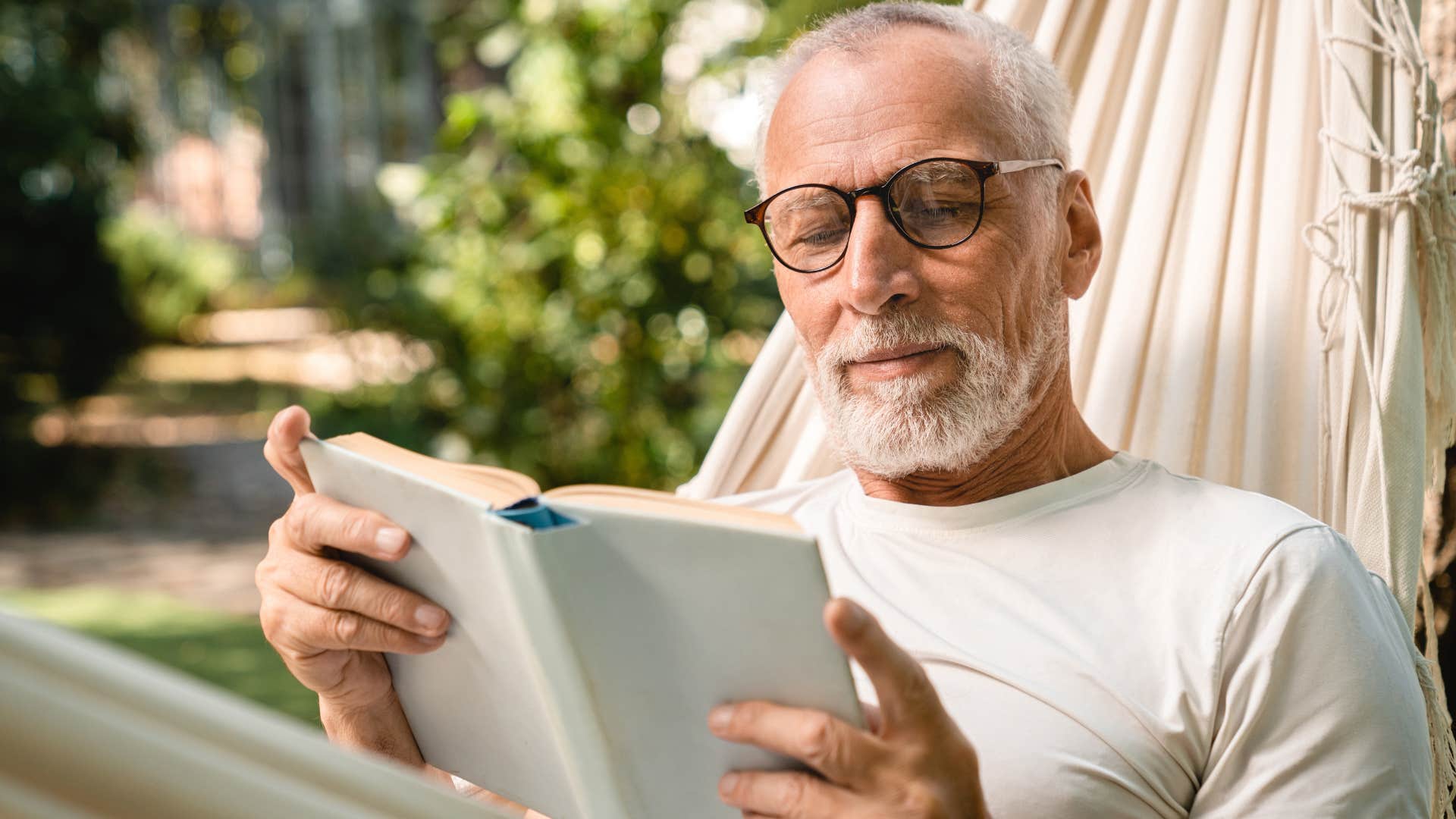 Man smiling and reading in a hammock.