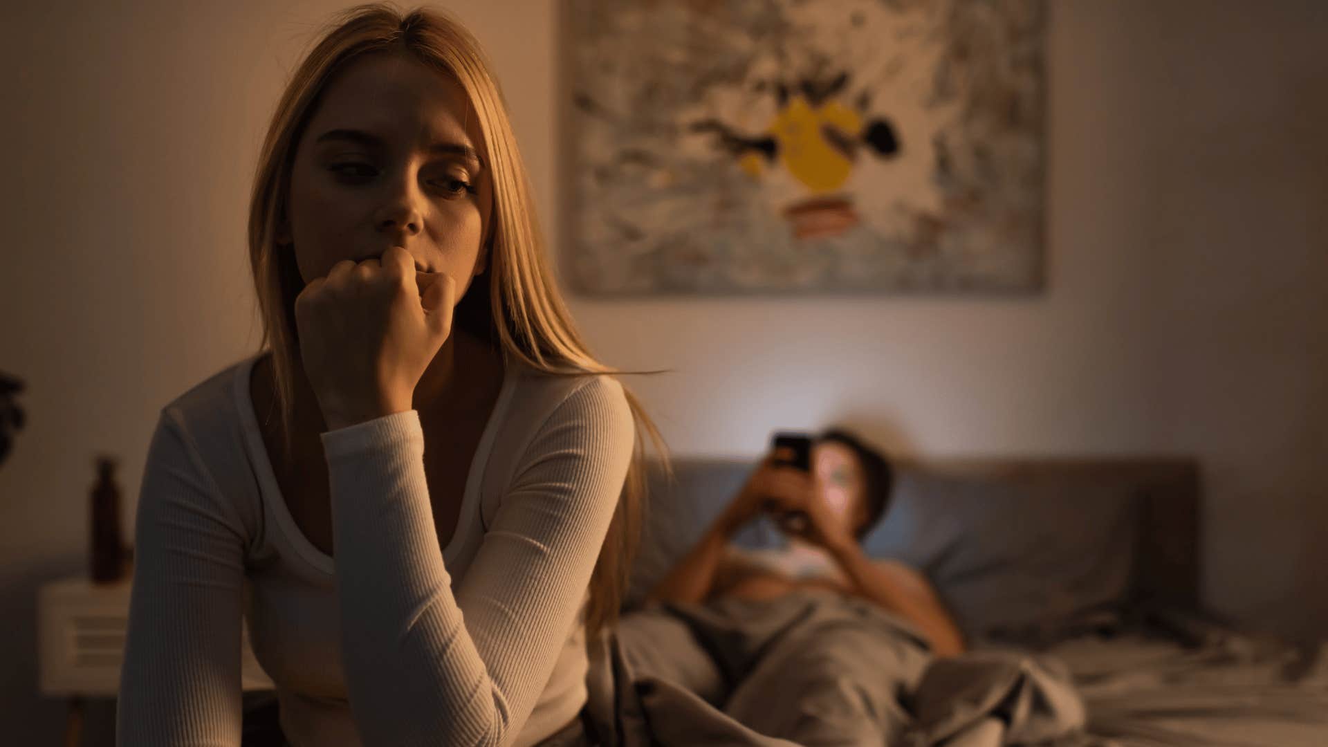 woman on bed with man on phone behind her