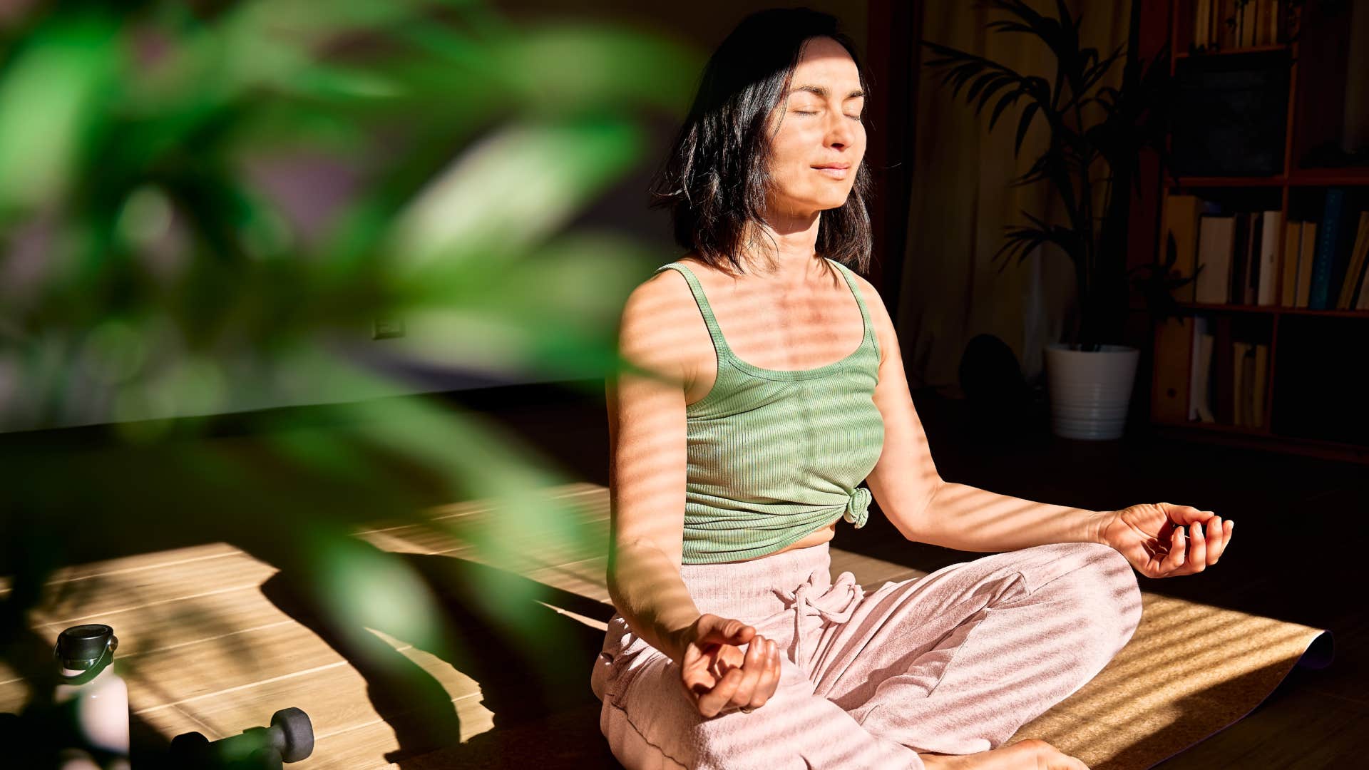 Woman practicing yoga and meditation at home sitting in lotus pose on yoga mat