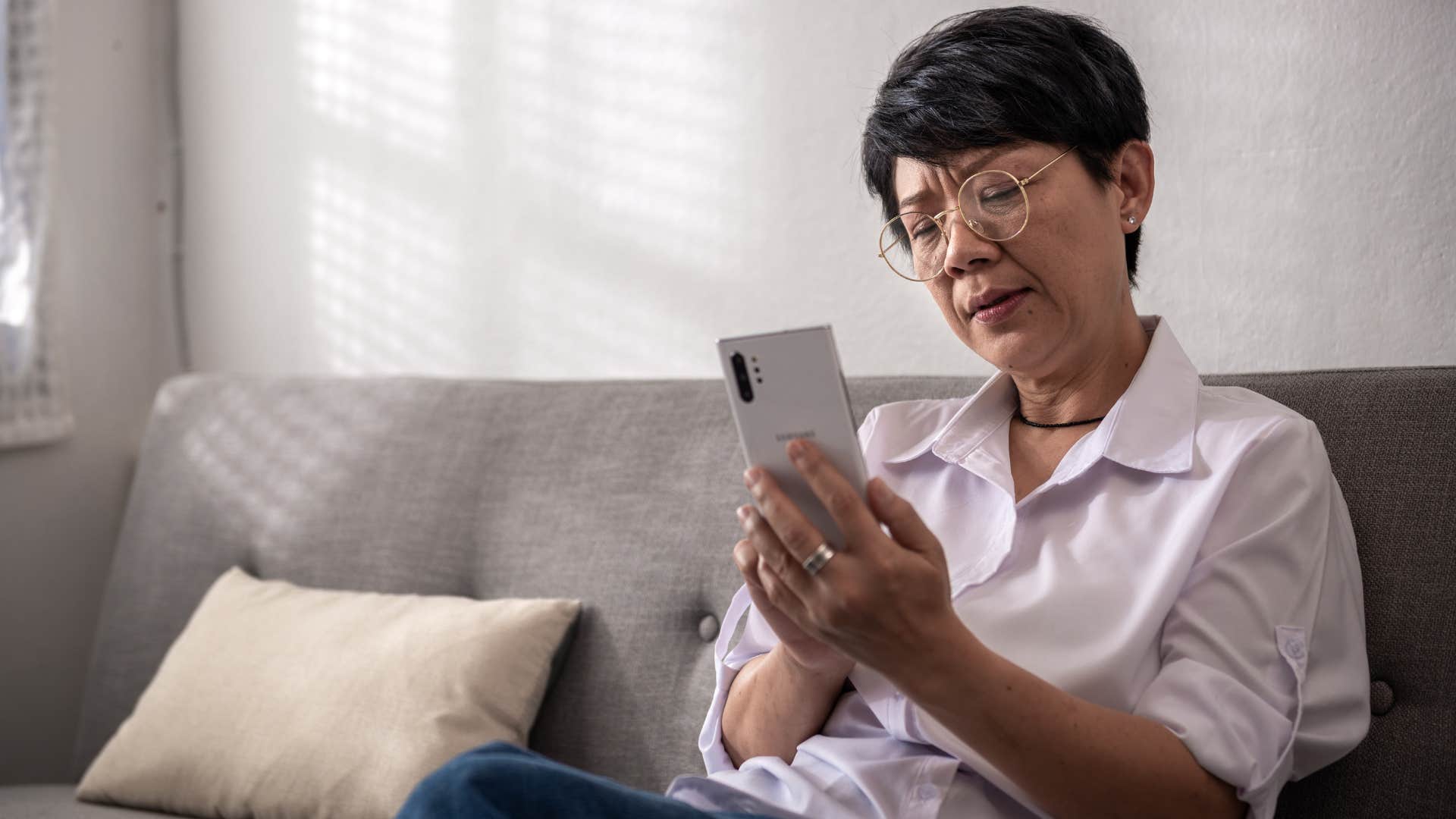 Older woman looking upset texting on her phone.