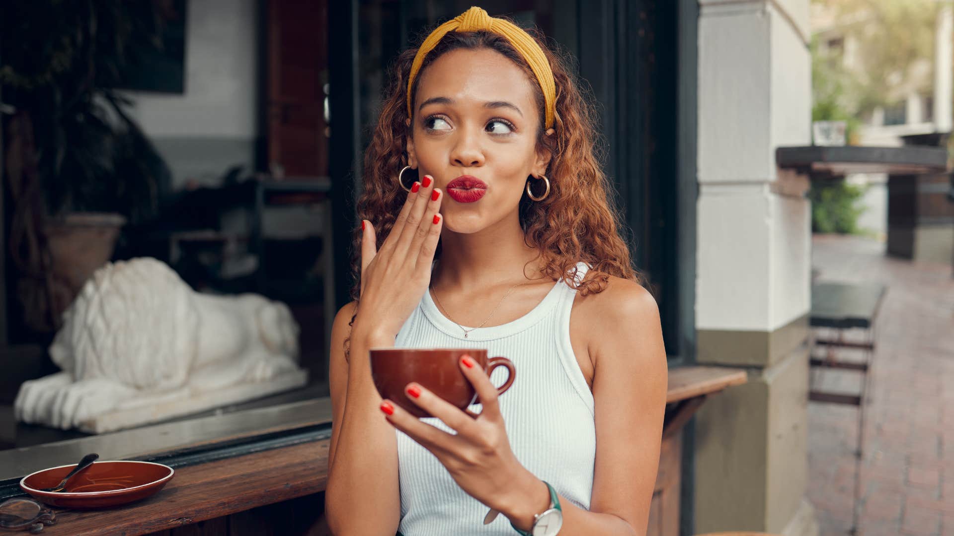 Coffee, cafe and hand of a black woman with funny face while sitting by a counter at an outdoor restaurant.