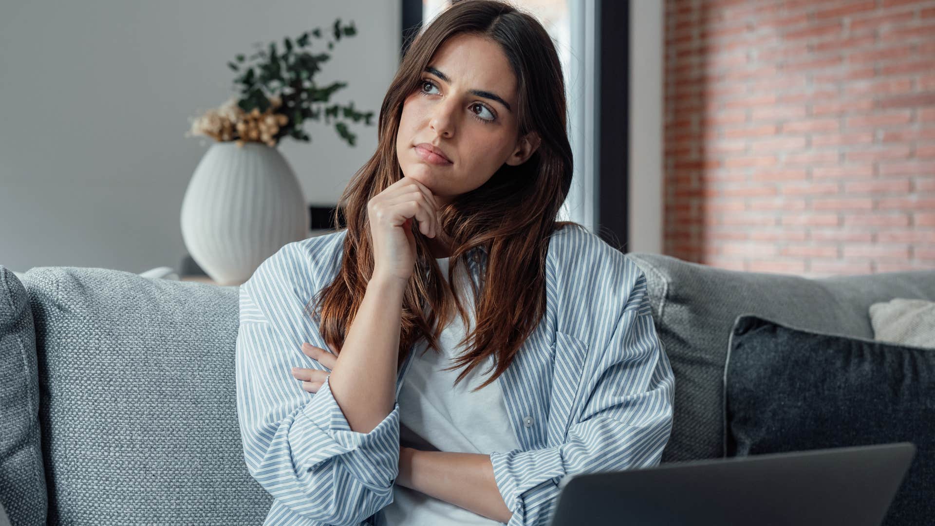 Young woman holding her chin while sitting on her couch.