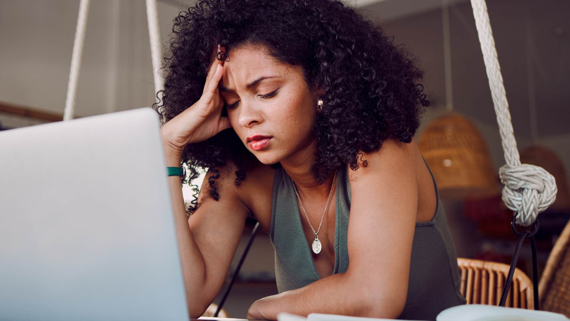 Tired young woman holding her head while working on her laptop.