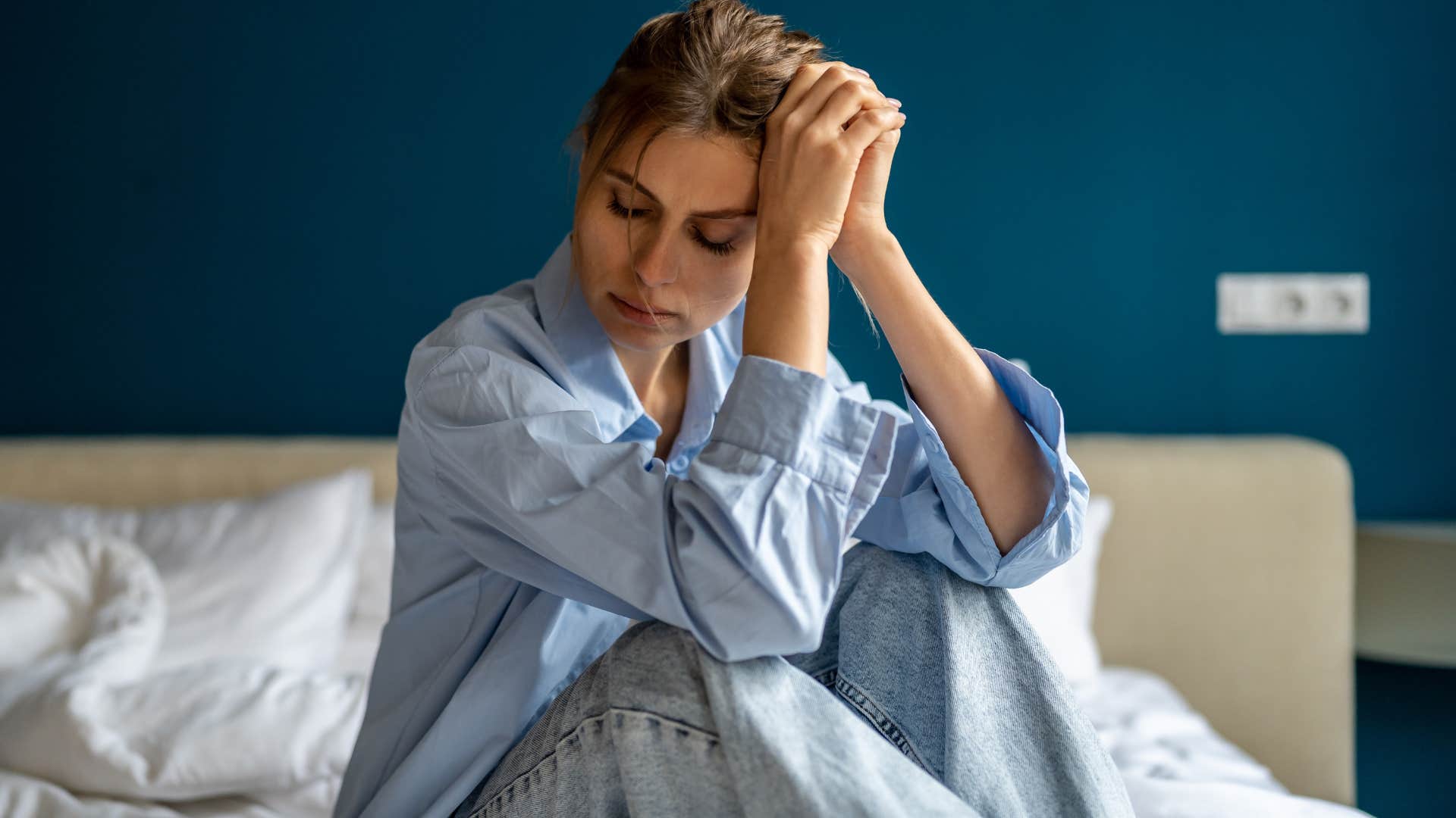 Woman looking tired sitting on her bed.