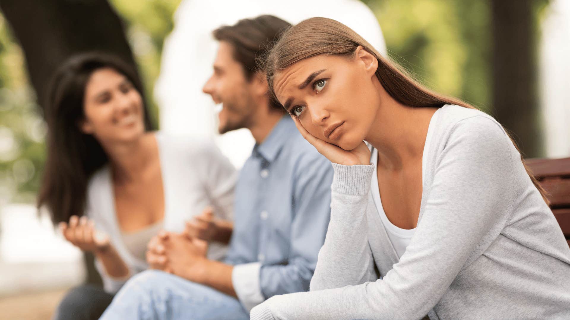 woman upset while man talks to another woman behind her