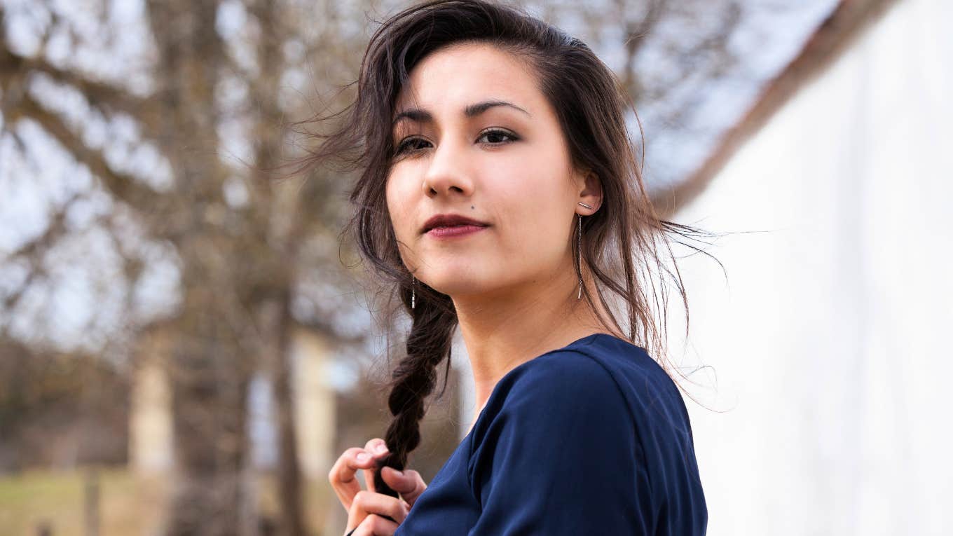 woman standing outside twirling hair and thinking