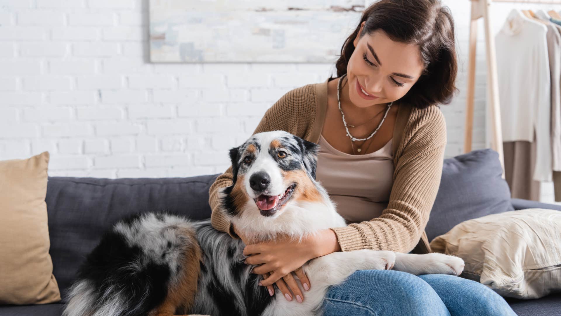 happy young woman cuddling australian shepherd dog while sitting on couch