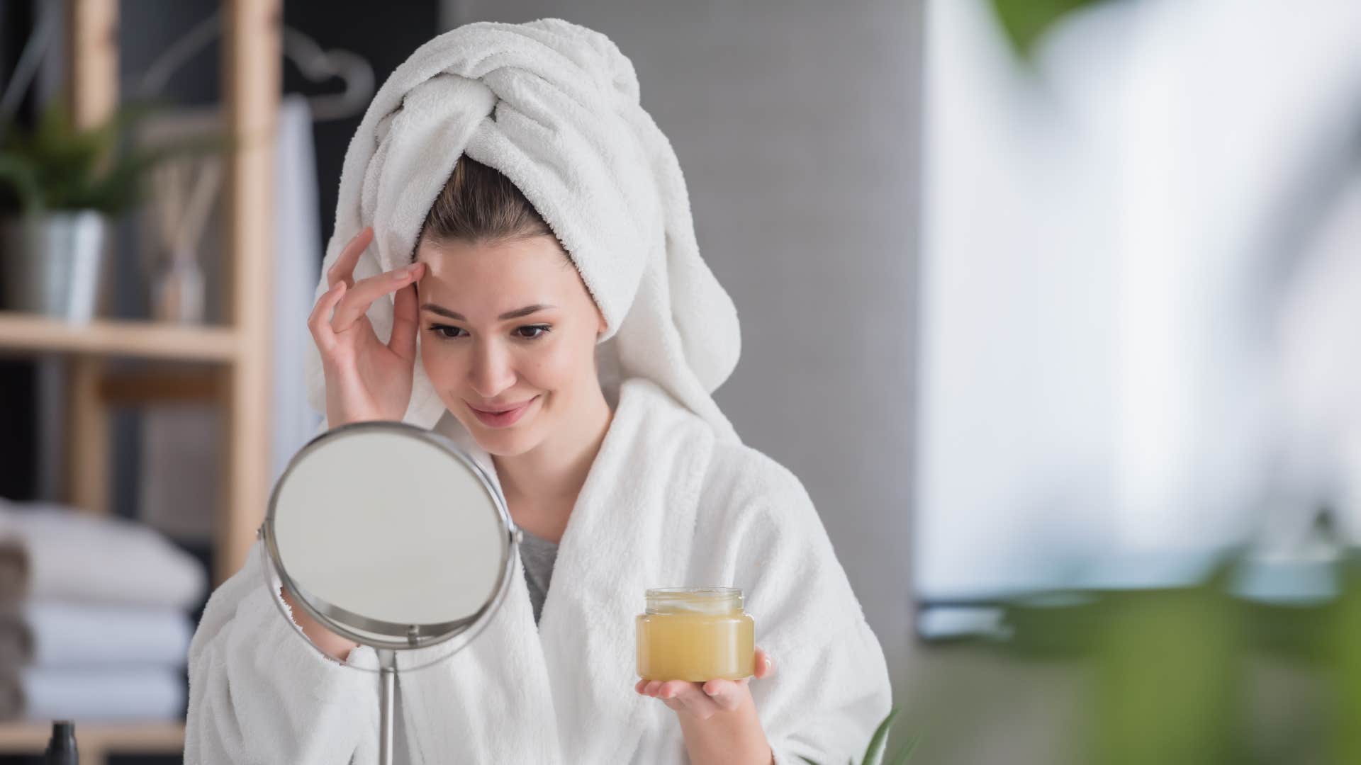 Portrait of a young woman wearing a bathrobe at home doing her daily skincare routine with natural cosmetics