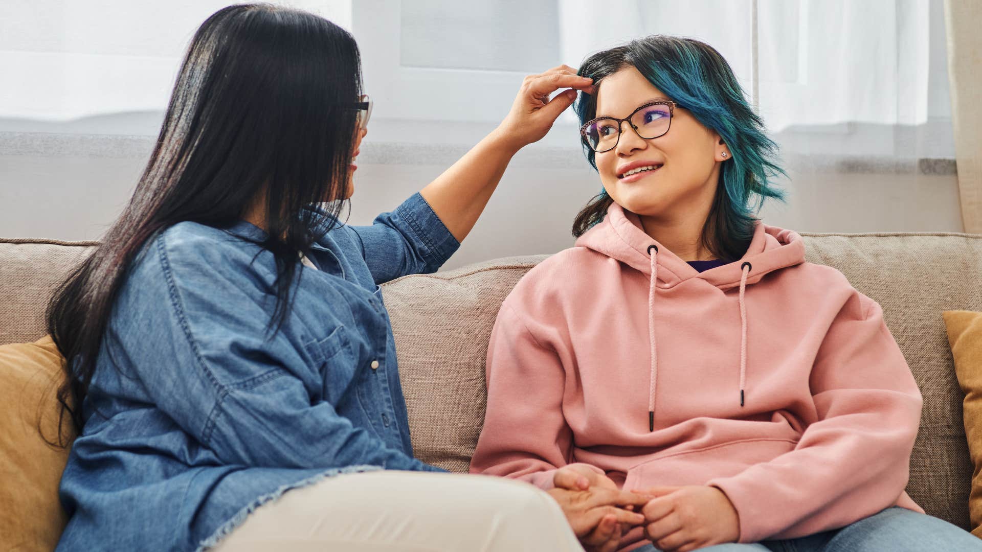 Woman touching her teenage daughter's hair and smiling.