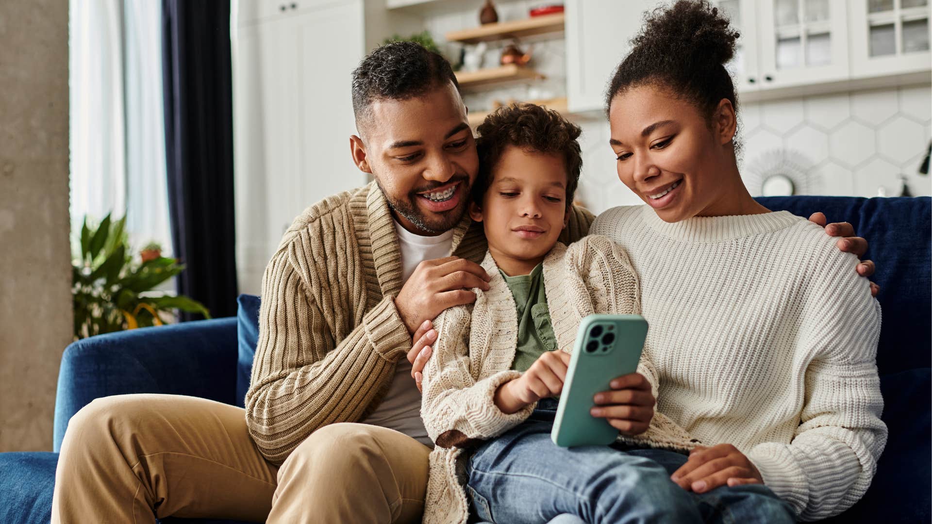 Young parents smiling and scrolling on a phone with their young daughter.