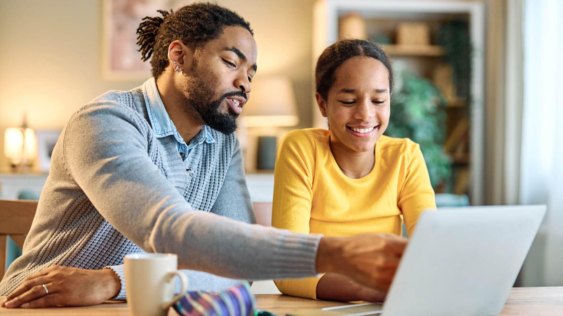 Dad showing his teenage daughter something on his laptop.