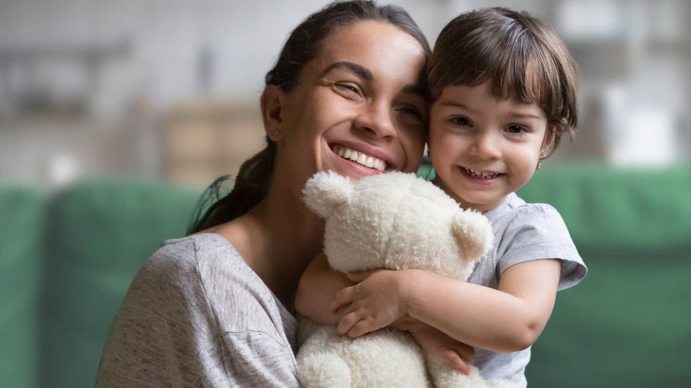 Gen Z woman hugging her young daughter on the couch.