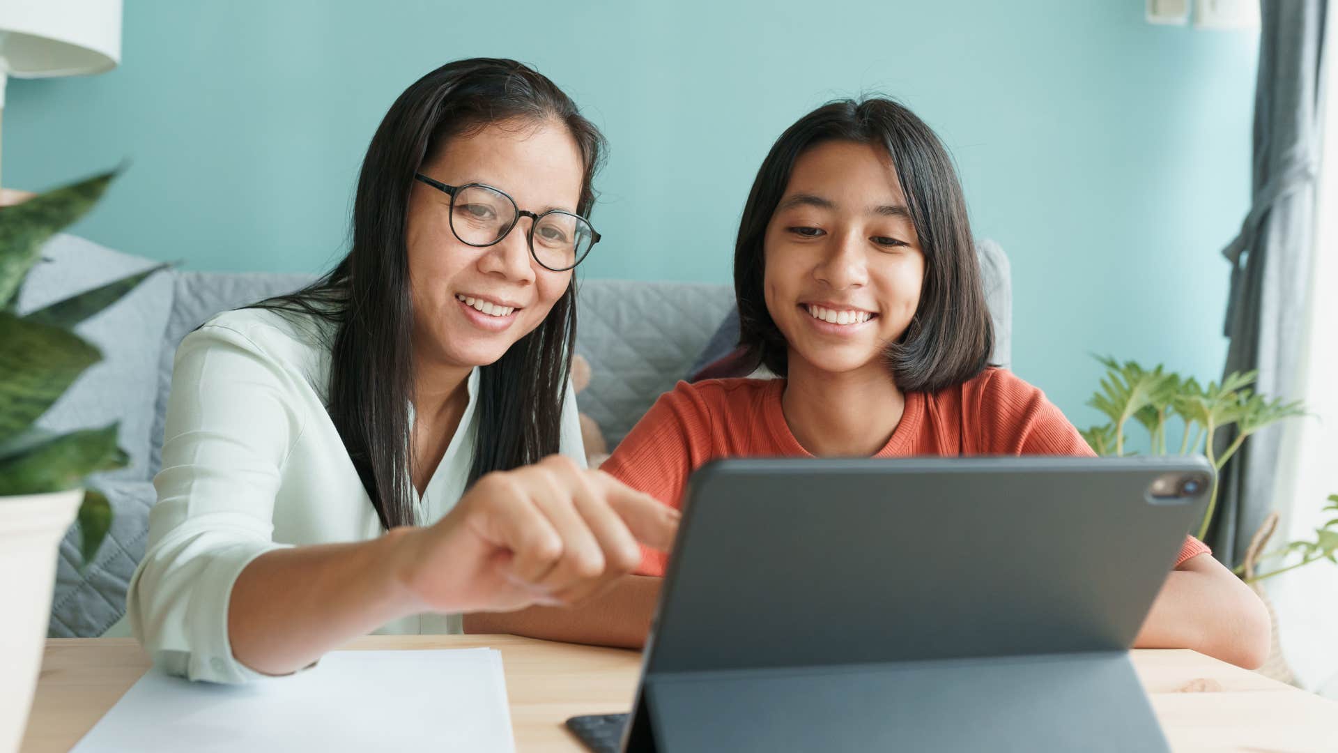 Mother smiling and looking at a tablet with her daughter.