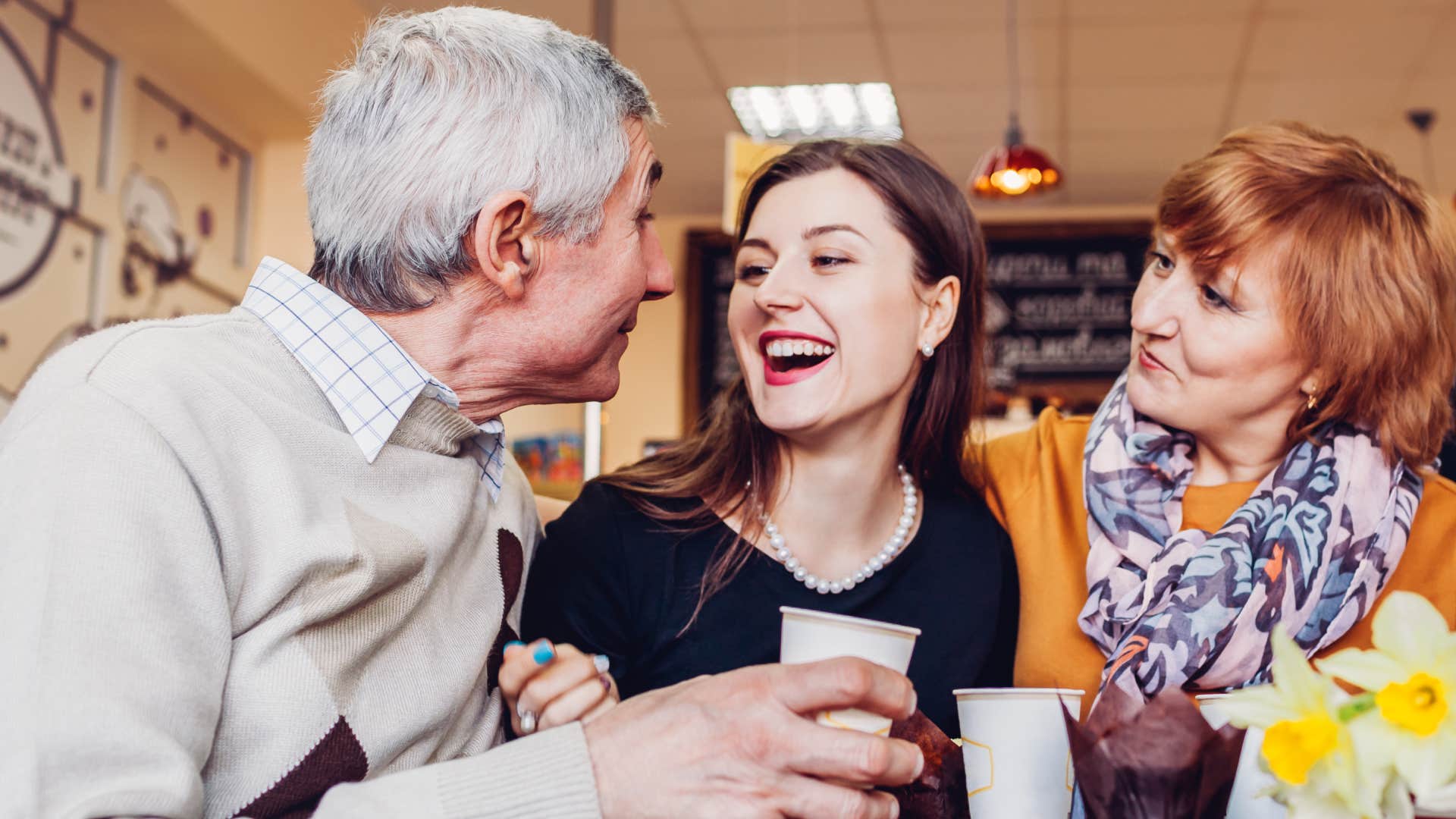 couple with adult daughter chat and laugh in cafe