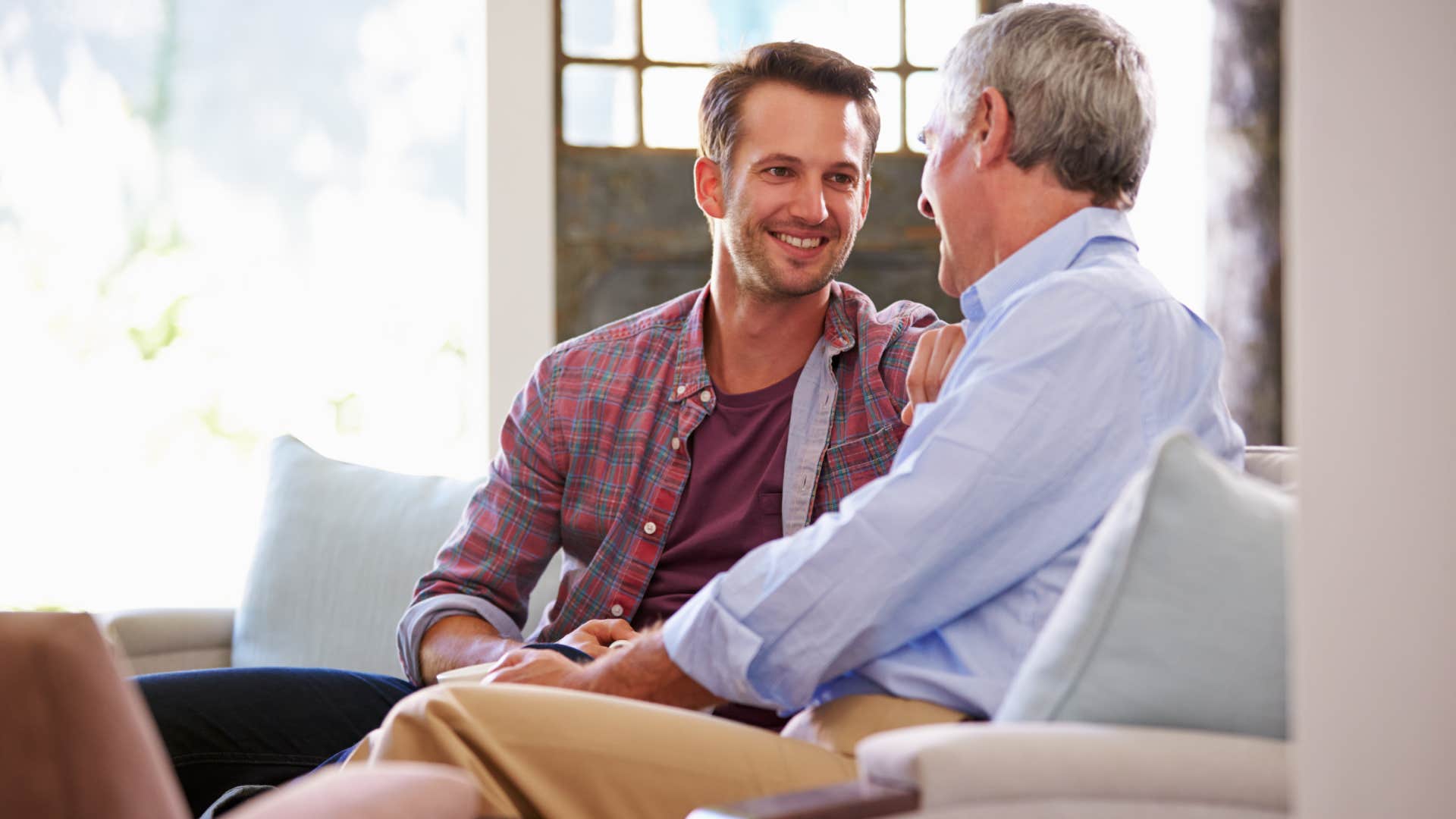 senior father with adult son relaxing on sofa at home