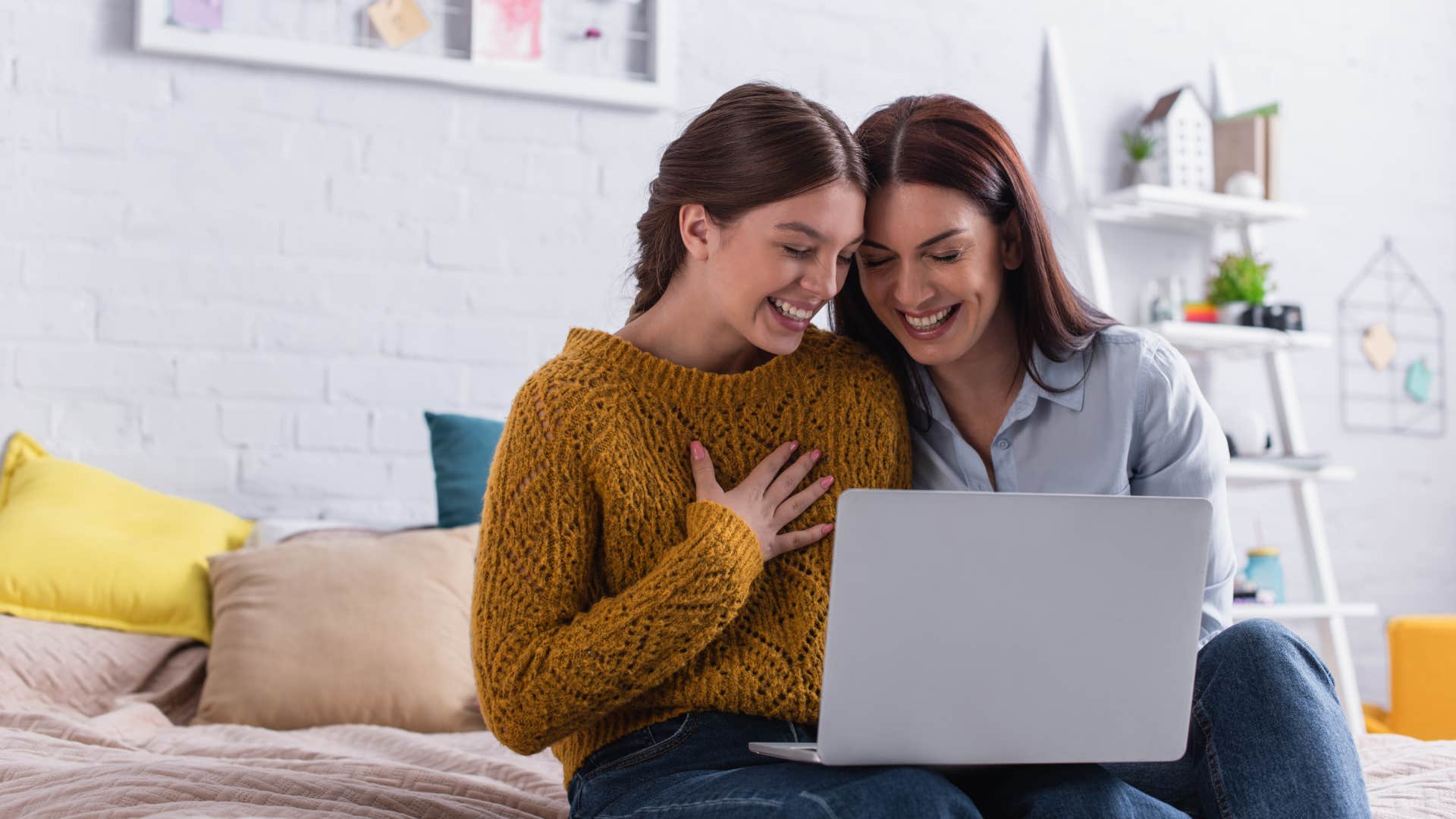 happy teenage girl and mother watching comedy movie on laptop in bedroom